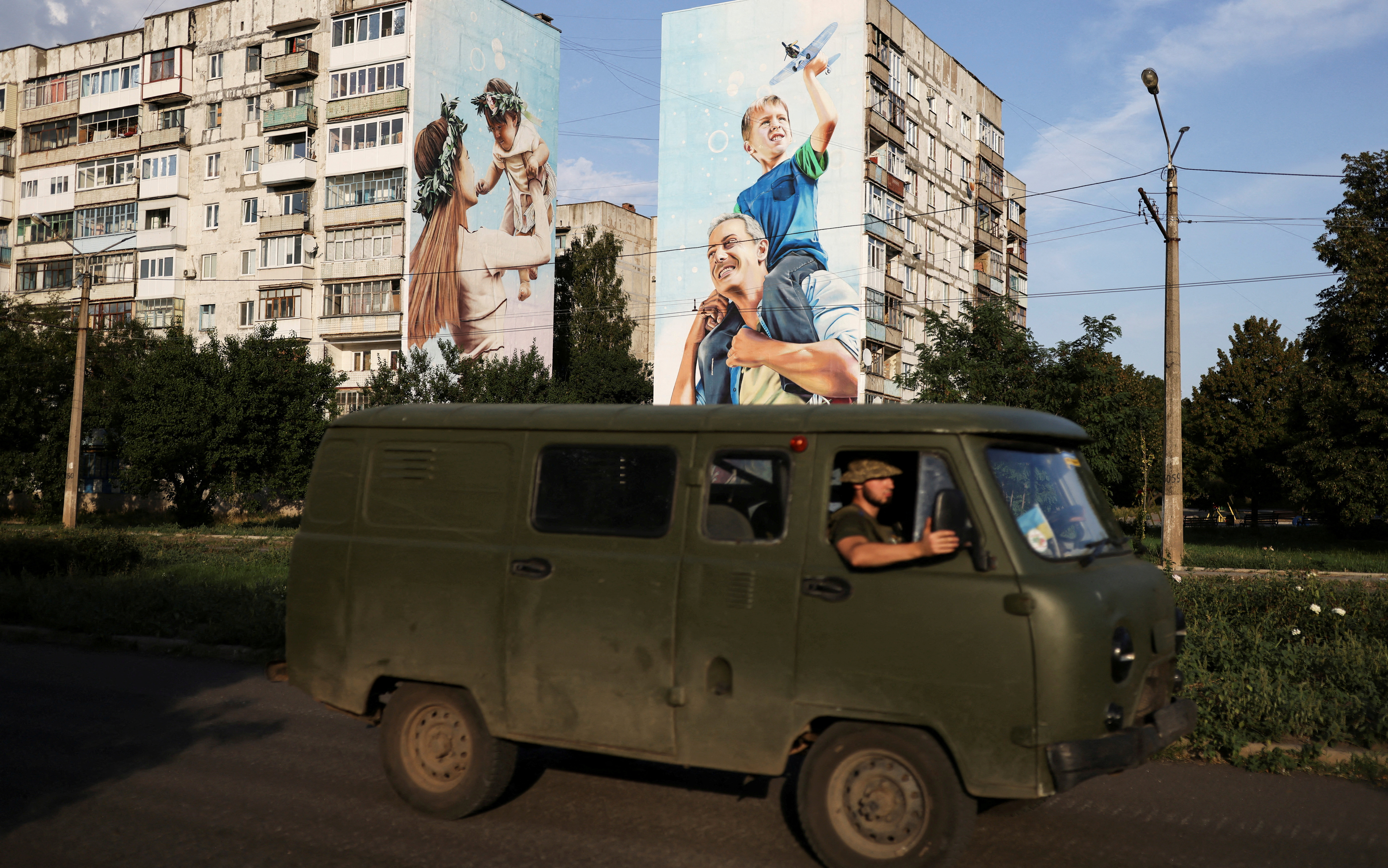Ukraine servicemen drive past a mural of a family on damaged buildings in Bakhmut
