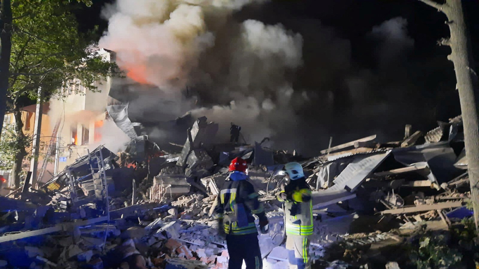 Emergency workers look at a burning building in Kharkiv, Ukraine, as plumes of smoke rise into the night sky