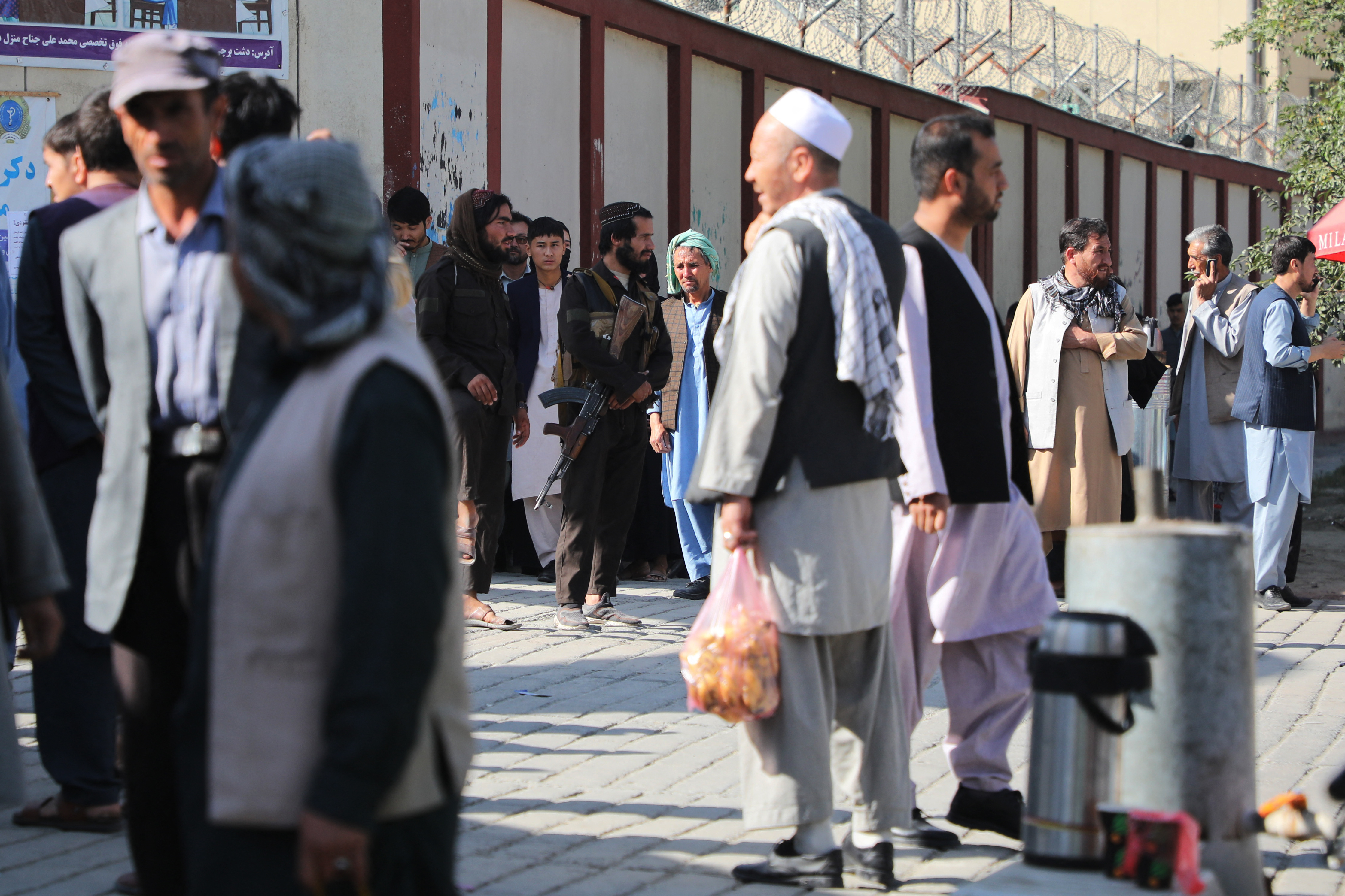 Taliban fighters stand guard as people gather to search for relatives outside a hospital in Kabul after an attack on an education centre in the Dasht-e-Barchi area of Afghanistan’s capital [AFP]