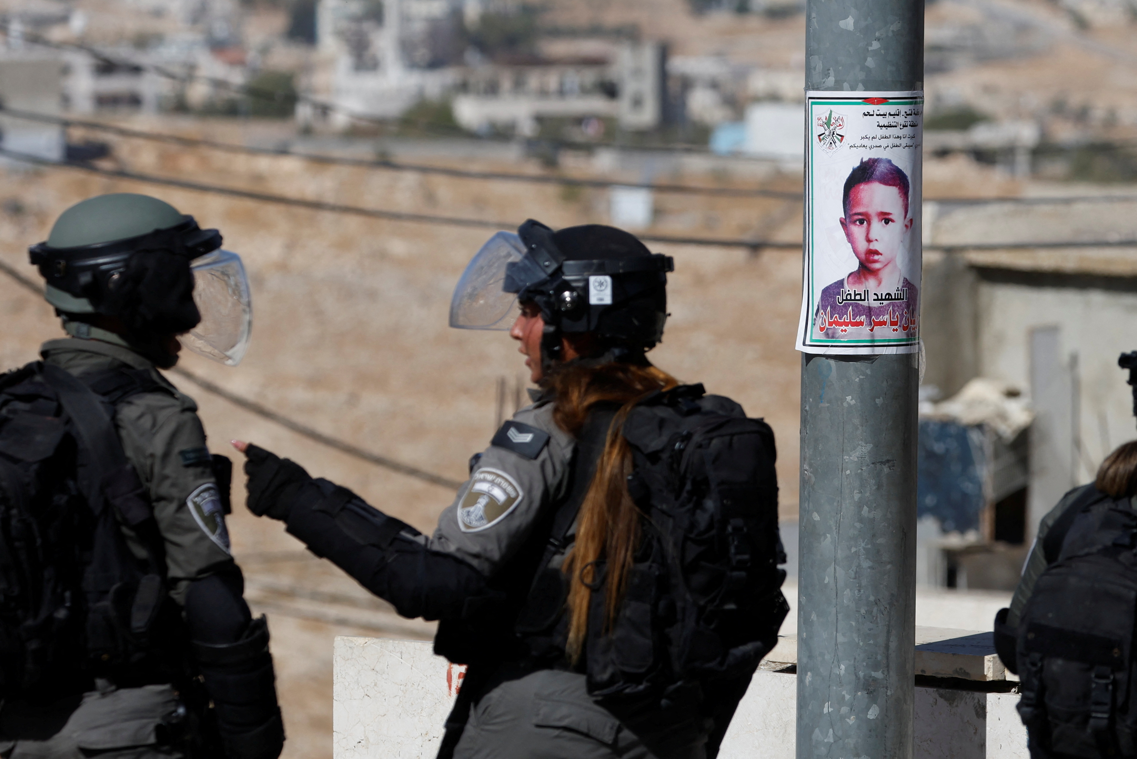 Israeli forces stand next to a picture of seven-year-old Palestinian boy Rayan Suleiman, who according to his father has died of heart failure after being chased by Israeli soldiers