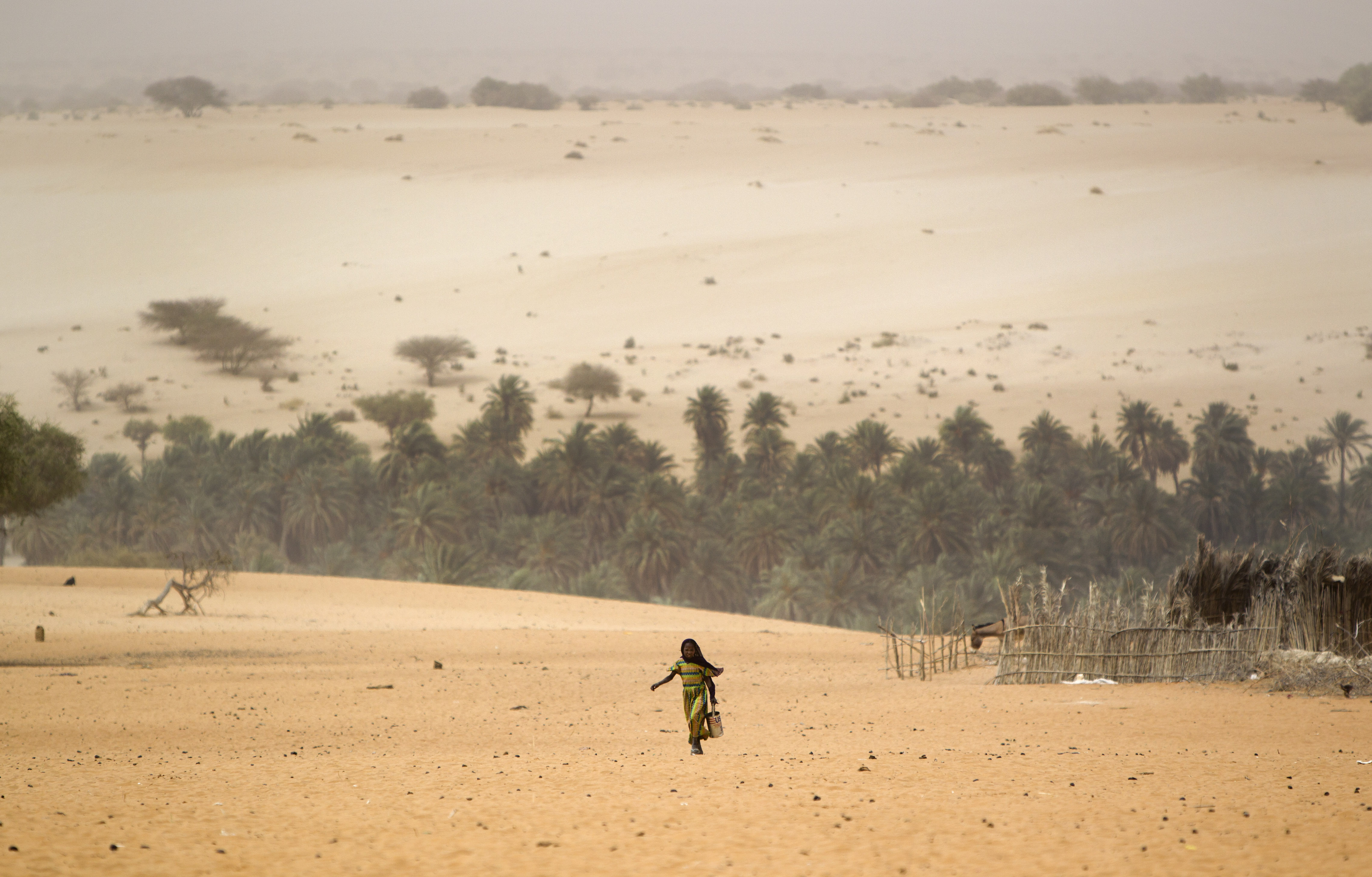 A young girl carries an empty container as she walks across the sands to fill it from a well in Barrah, a desert village in the Sahel belt of Chad