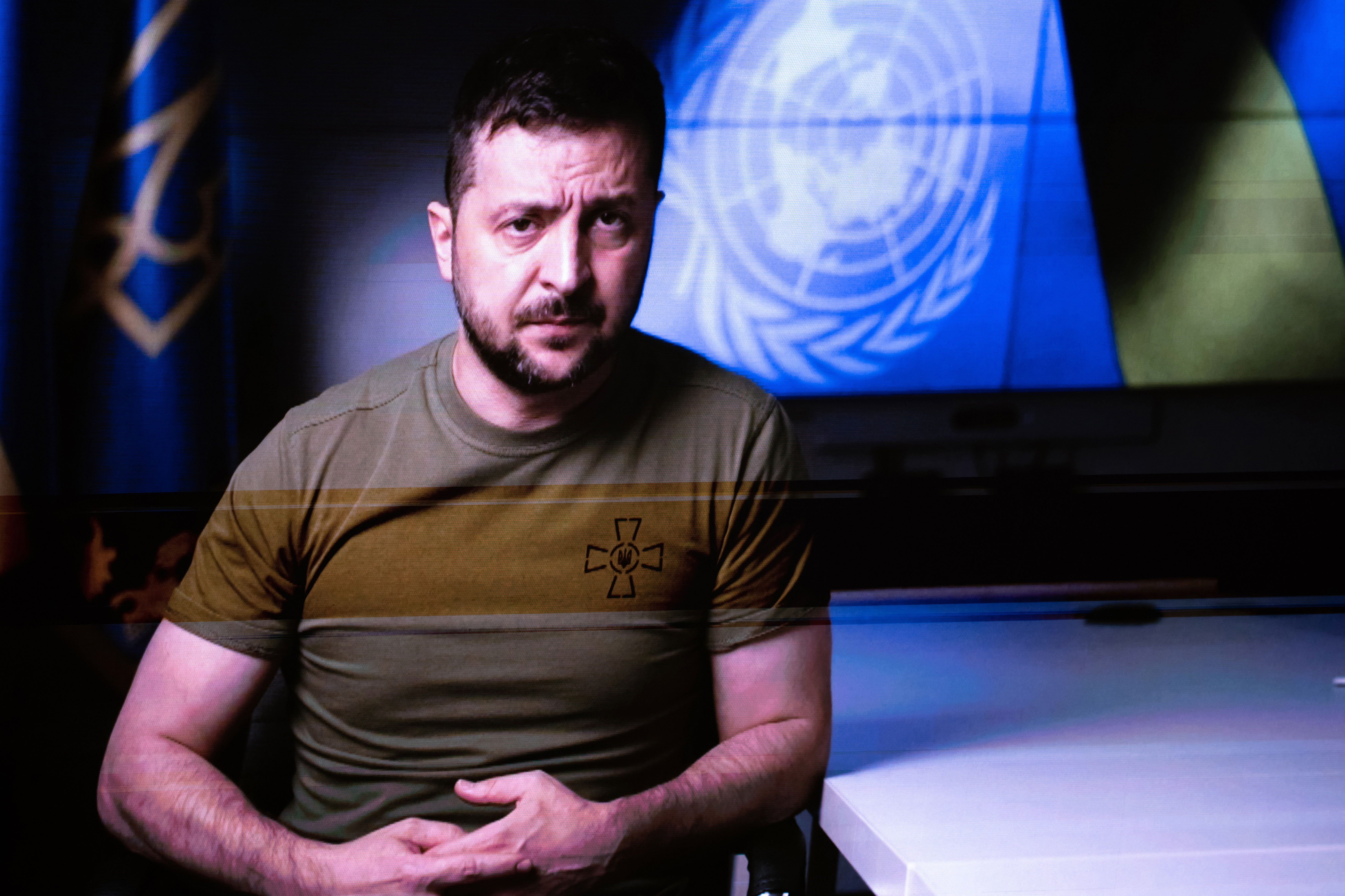 Volodomyr Zelenskyy in trade mark khaki green t-shirt with a Ukraine flag and UN logo behind him addresses the UN General Assembly in a video speech.