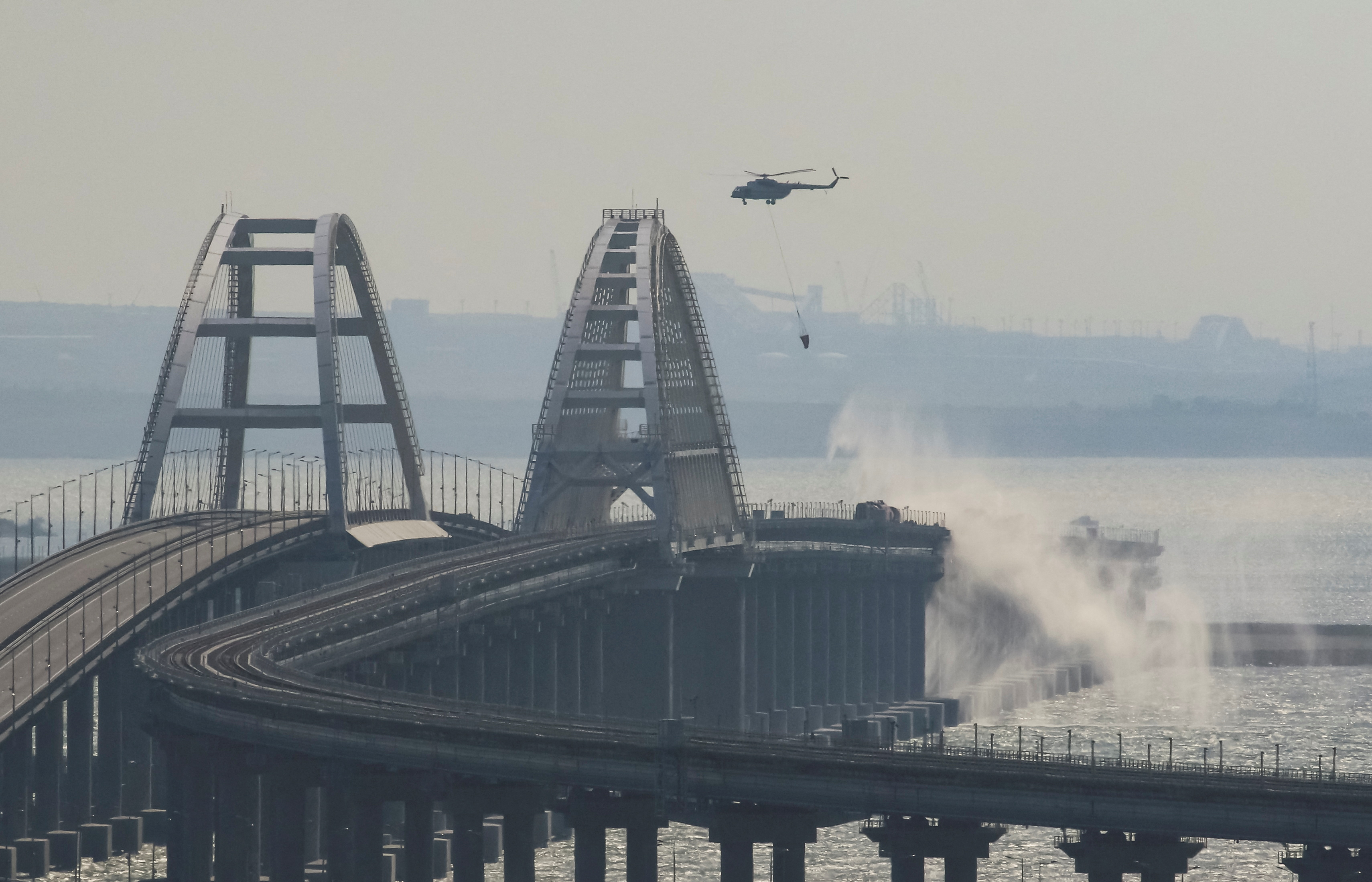 A helicopter drops water to extinguish fuel tanks ablaze on the Kerch bridge in the Kerch Strait, Crimea, October 8, 2022. REUTERS/Stringer