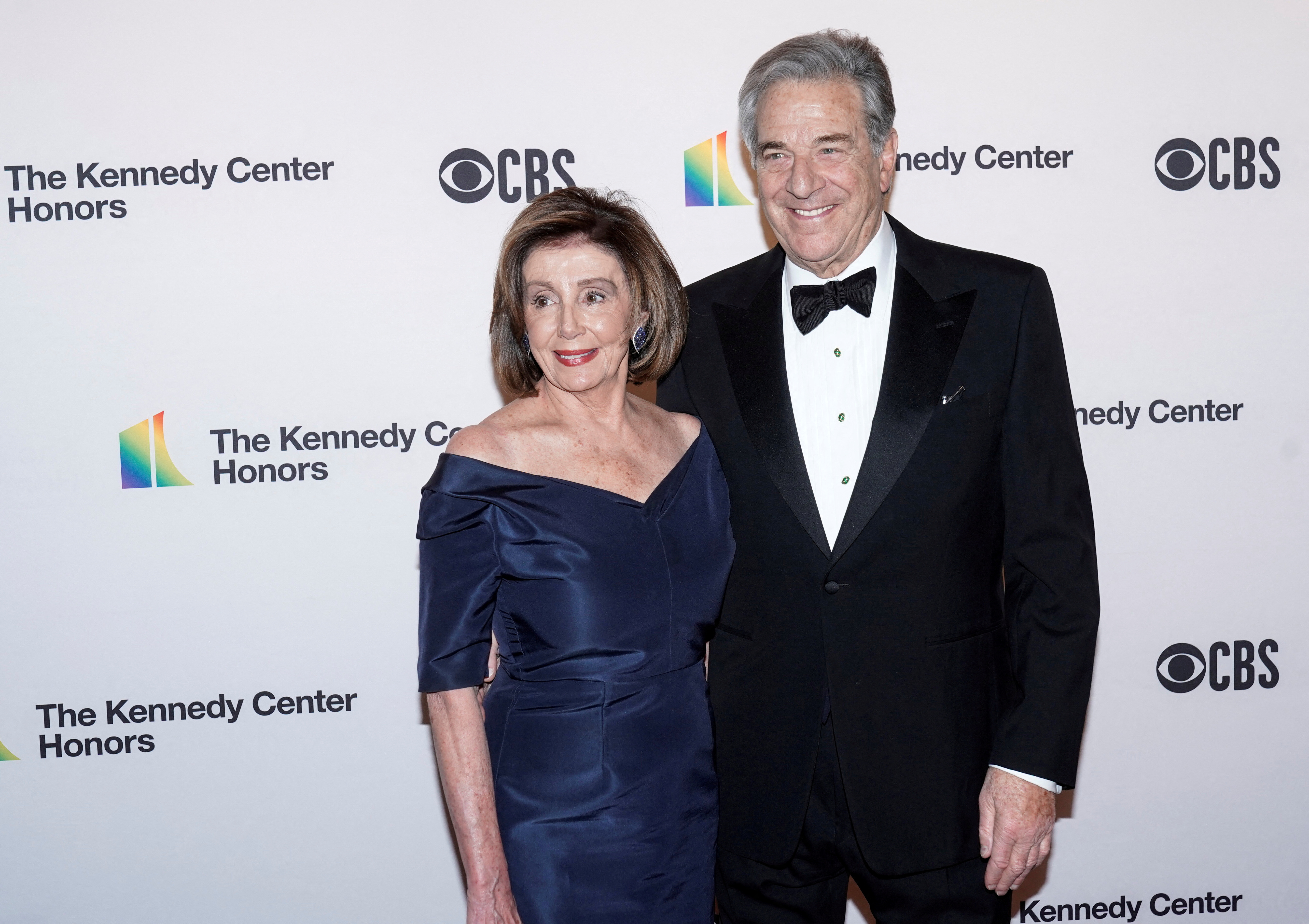 Nancy (in blue dress) and Paul (in black tux) Pelosi with arms around each other posing for photo