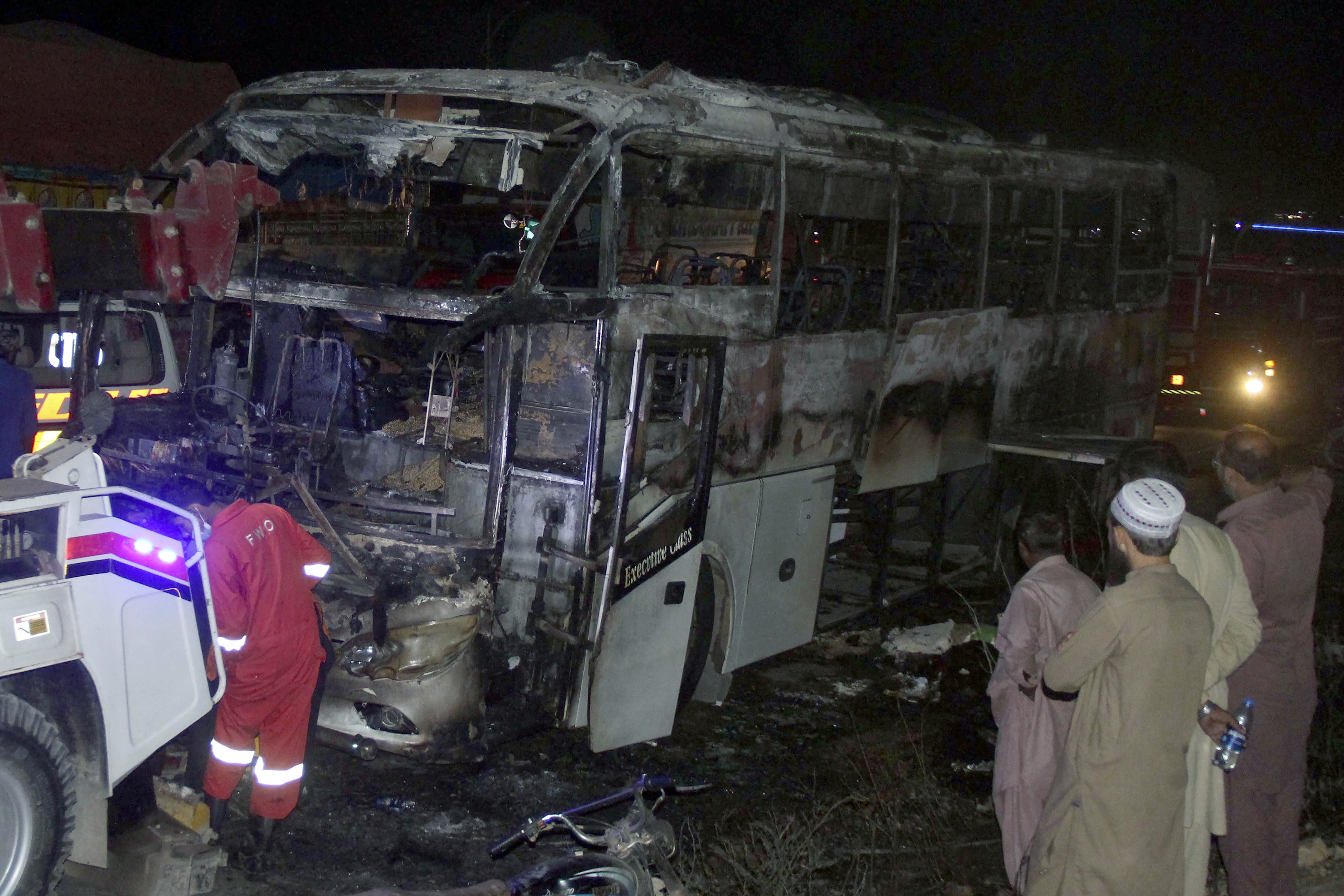 Volunteers gather beside a charred bus on a highway in Nooriabad, Pakistan