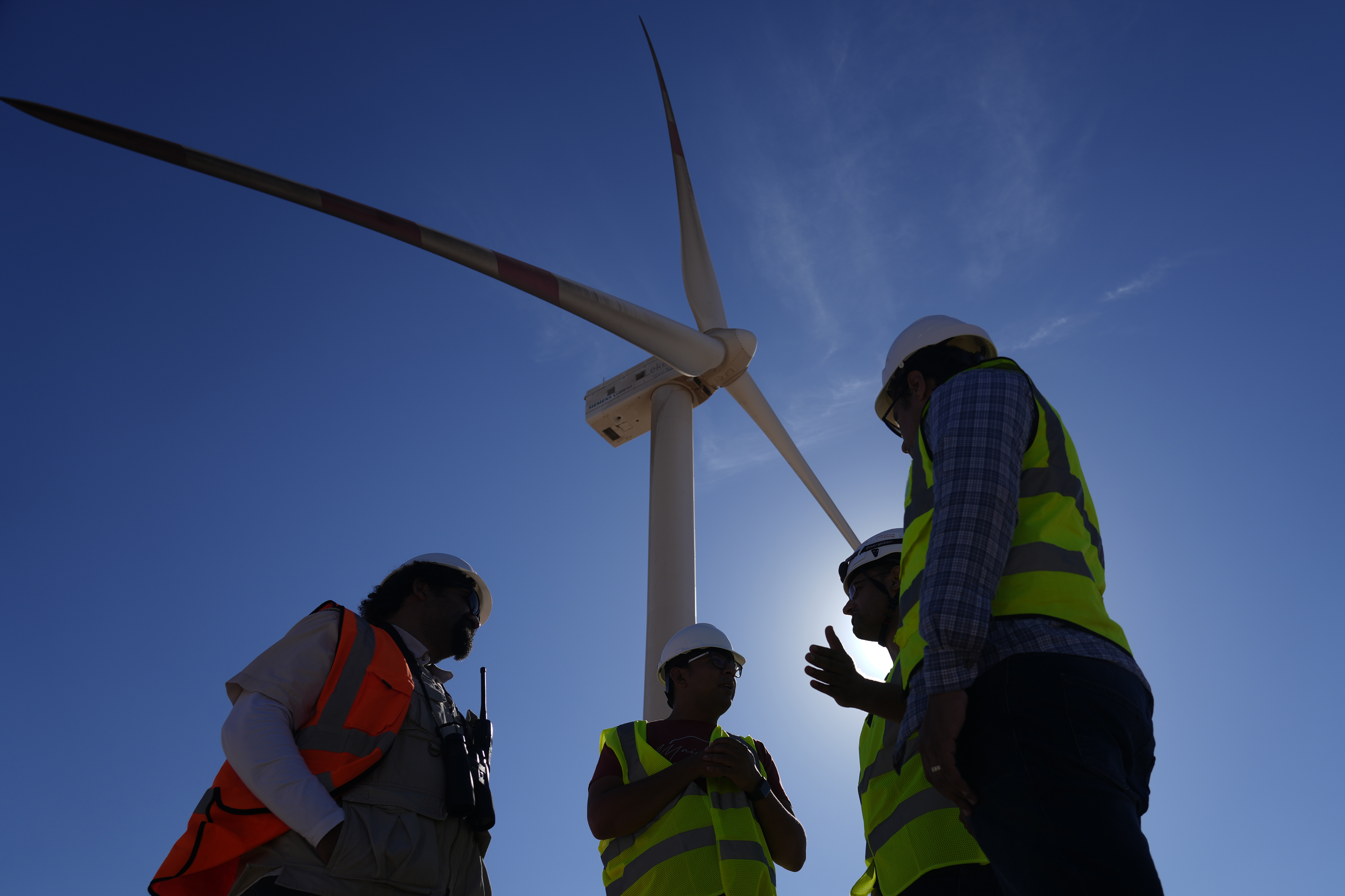 FILE - Engineers chat under a wind turbine at Lekela wind power station, near the Red Sea city of Ras Ghareb some 300 km (186 miles), from Cairo, Egypt, Wednesday, Oct. 12, 2022. Spiraling energy costs caused by various economic factors and the Ukraine war could be a turning point toward cleaner energy, the International Energy Agency said in a report Thursday, Oct. 27. It found the global demand for fossil fuels, including coal, oil, and natural gas, is set to peak or plateau in the next few decades. (AP Photo/Amr Nabil, File)