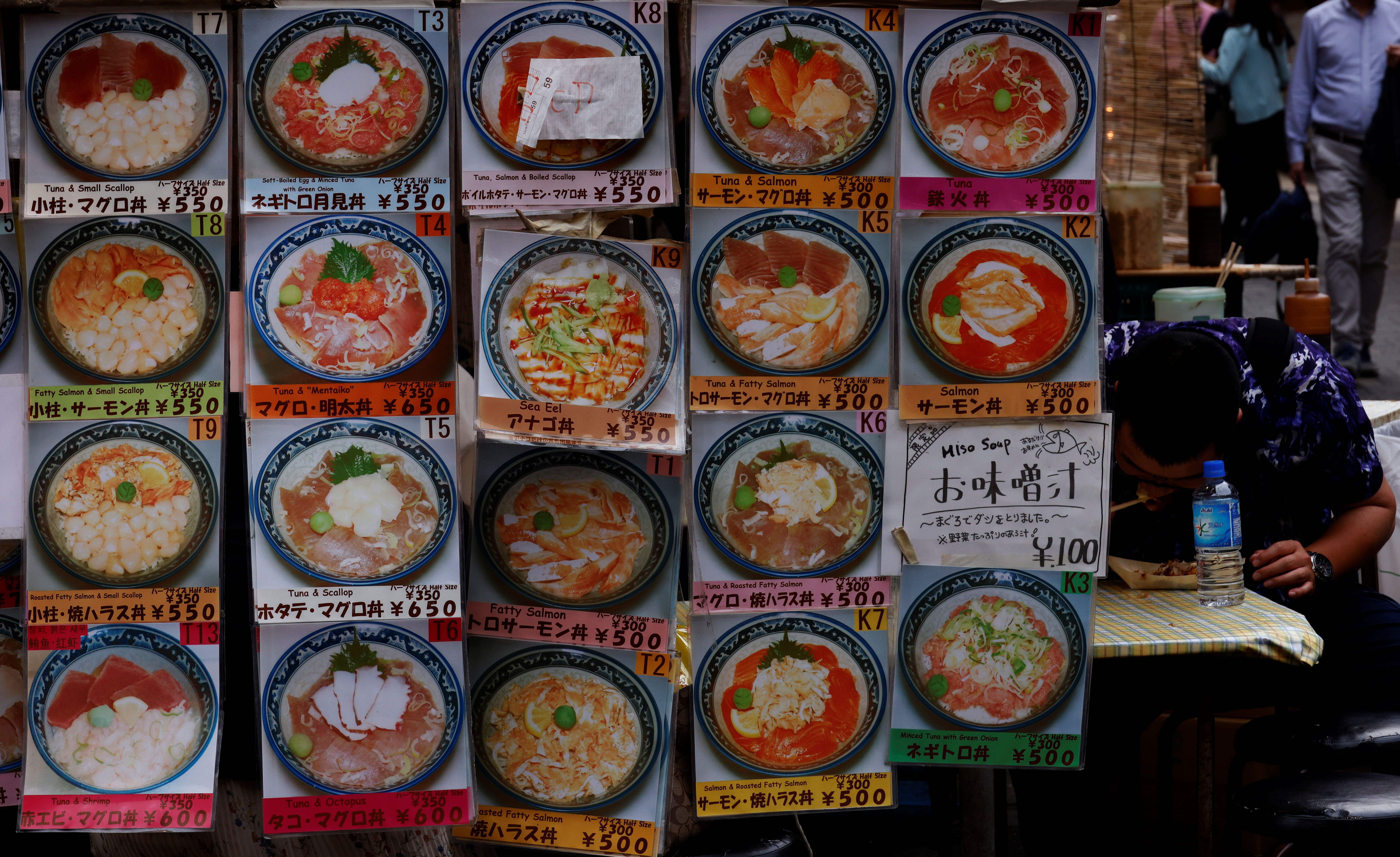 Window of restaurant in Japan displaying menu: photos of dishes with prices. A man can be seen eating noodles inside