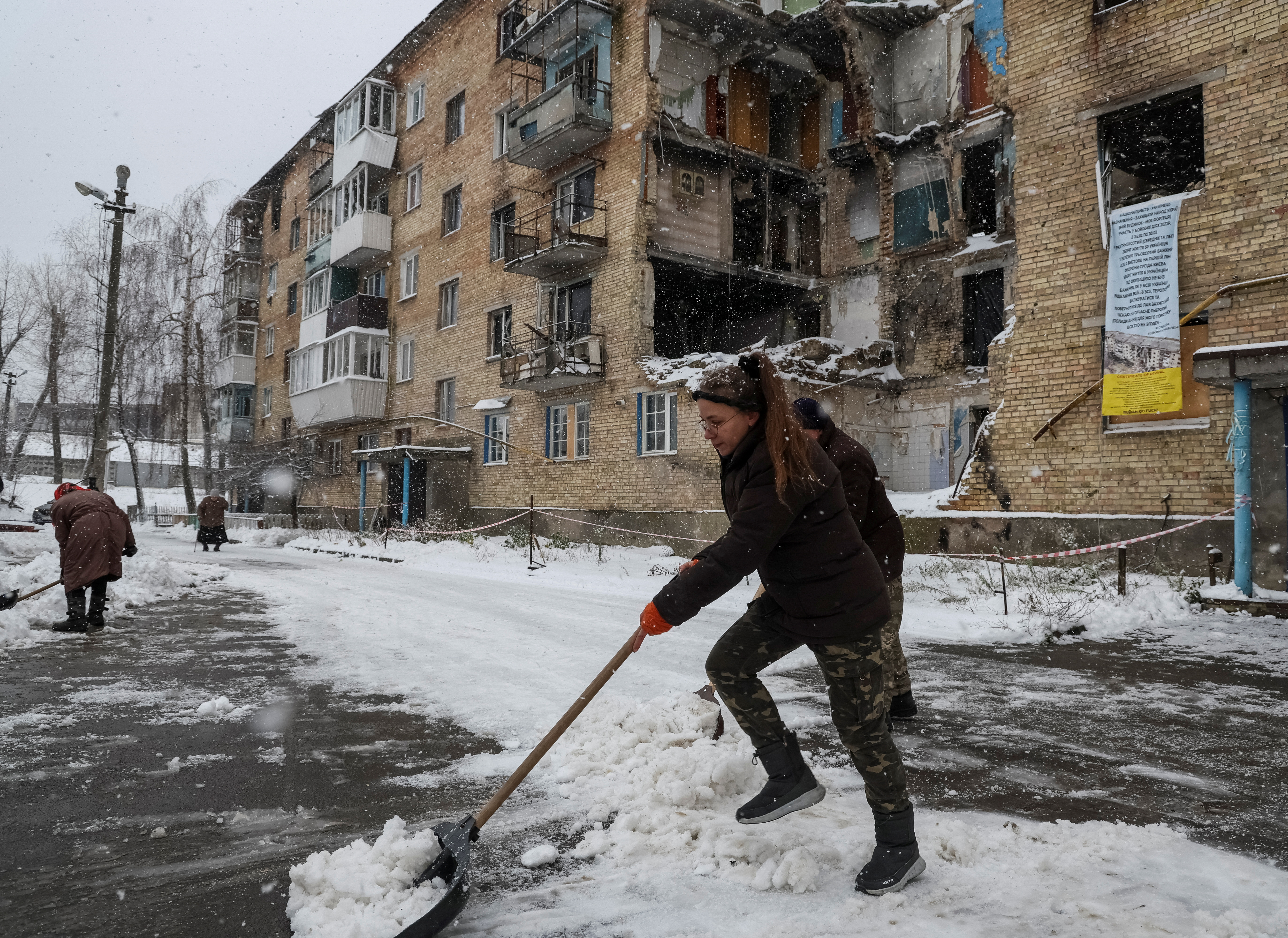 A woman shovelling snow in front of her apartment building which was badly damaged in Russian attacks