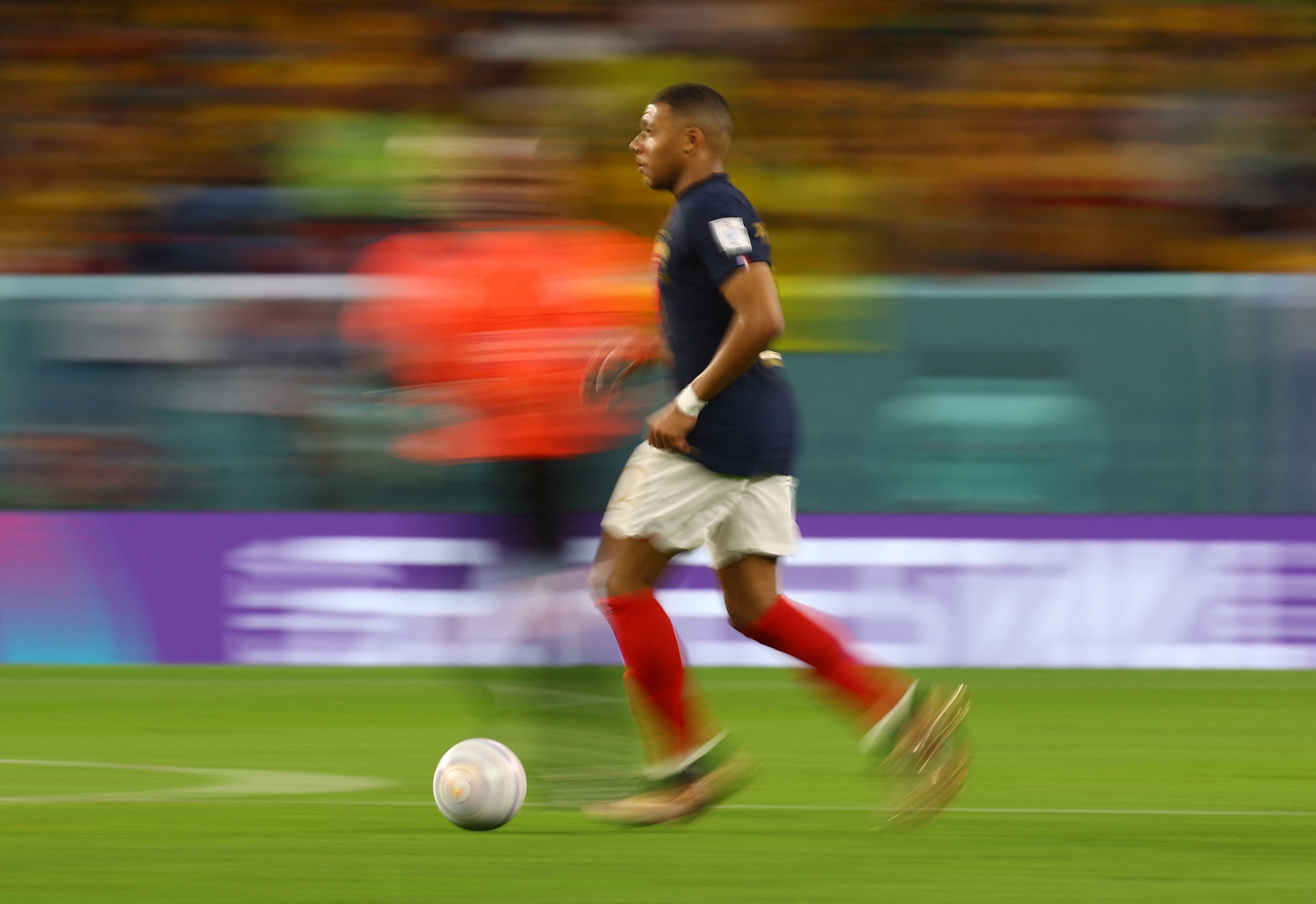 A motion blurred picture of Mbappe from the side as he moves across the field kicking a ball