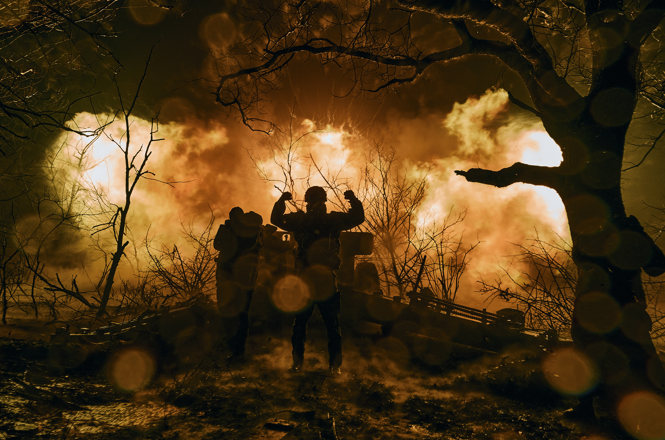 A Ukrainian soldier with his arms up in the air silhouetted against the flames of an explosion after firing artillery shells near Bakhmut, Ukraine.
