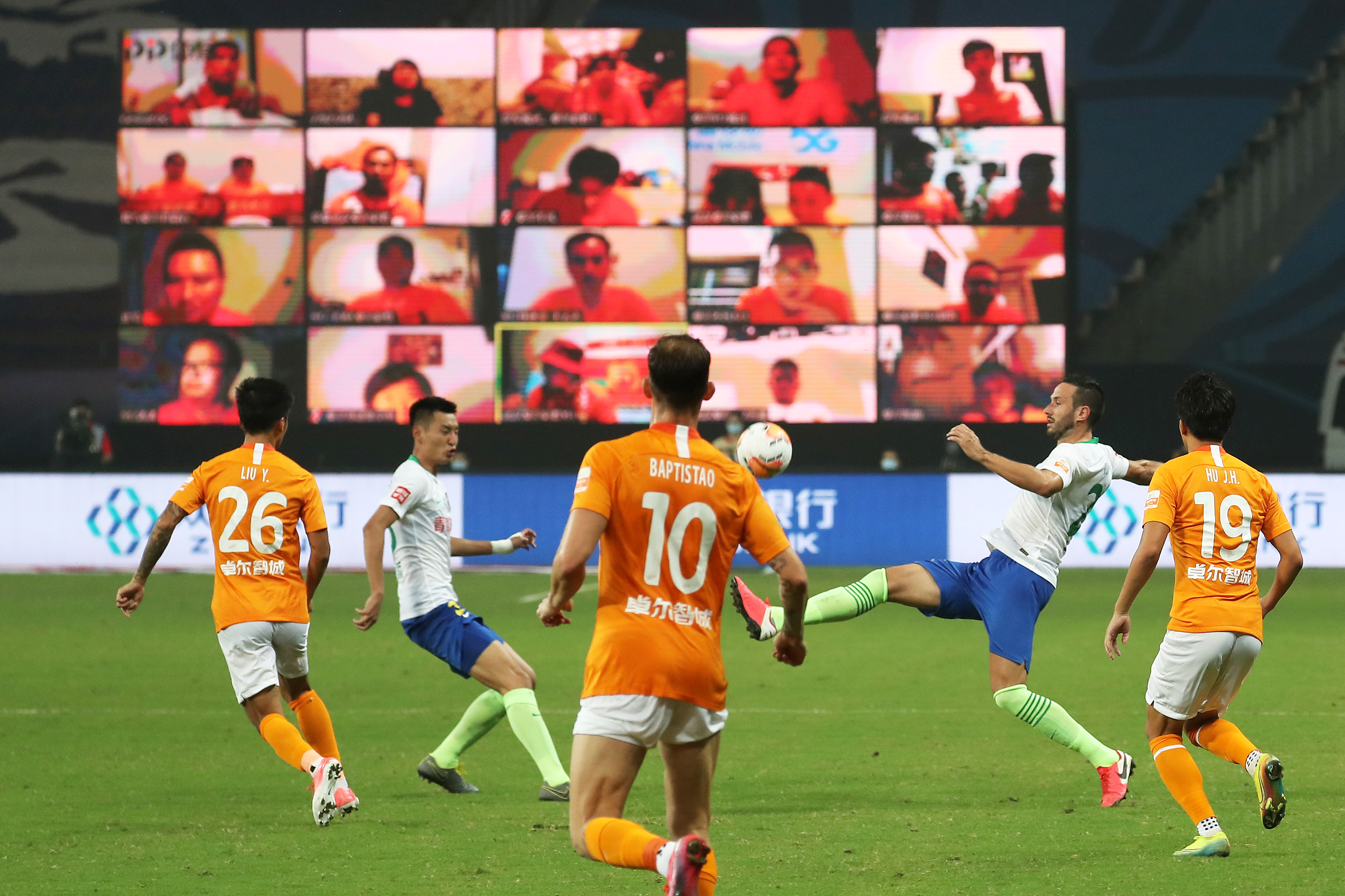 Soccer Football - Chinese Super League - Wuhan Zall vs Qingdao Huanghai - Suzhou, Jiangsu province, China - July 25, 2020. Players of Wuhan Zall in action against players of Qingdao Huanghai in front of a giant screen showing fans watching the match online, as it resumes following the coronavirus disease (COVID-19) outbreak. cnsphoto via REUTERS. ATTENTION EDITORS - THIS IMAGE WAS PROVIDED BY A THIRD PARTY. CHINA OUT.