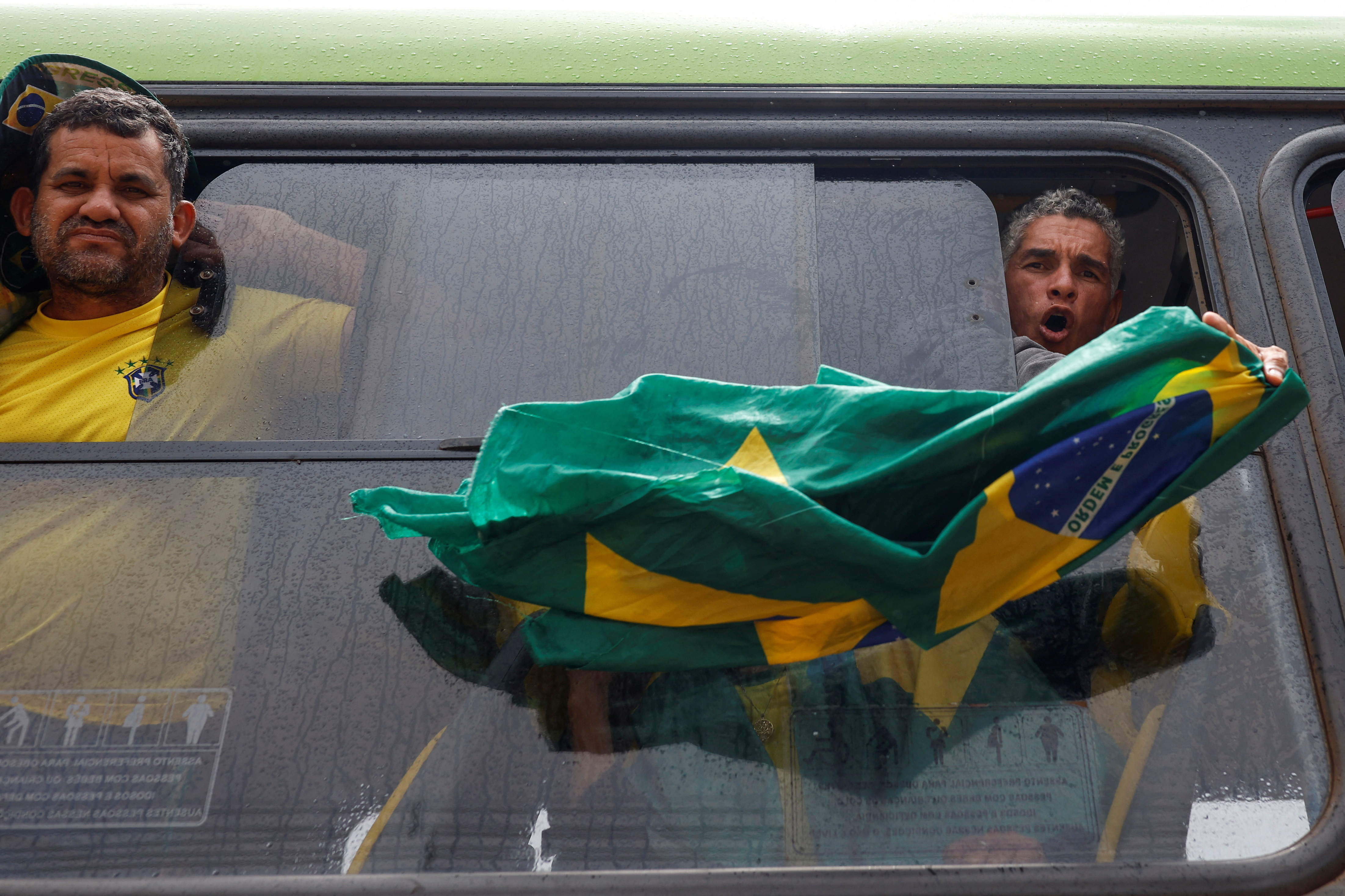 A man holds a Brazilian flag outside the window of a bus as he is detained after a camp set up by supporters of Brazil’s former President Jair Bolsonaro was dismounted in Brasilia on January 9, 2023