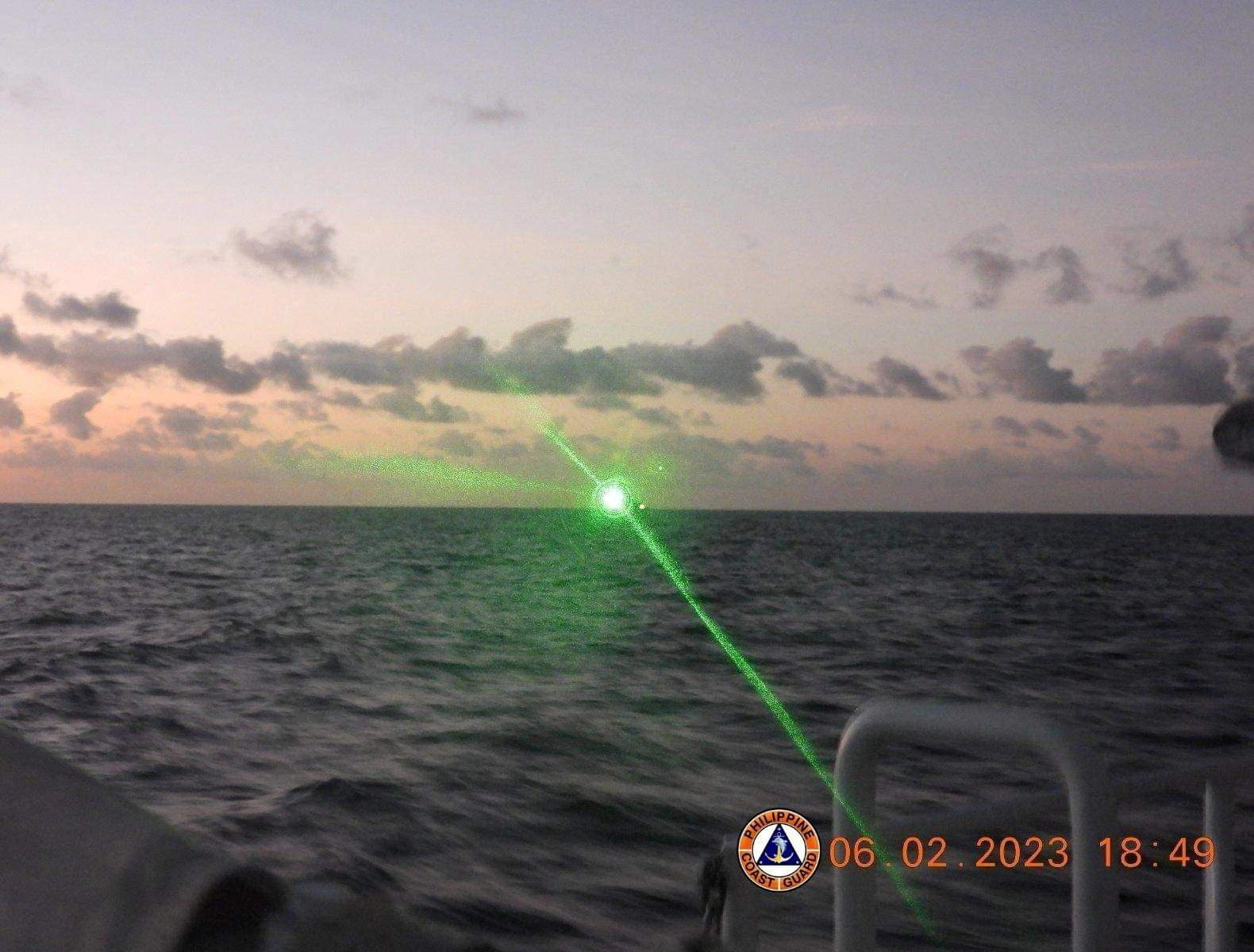 A bright green light coming from the direction of a Chinese Coast Guard ship near Second Thomas Shoal. It is nearly dark. The ship is silhouetted on the horizon.