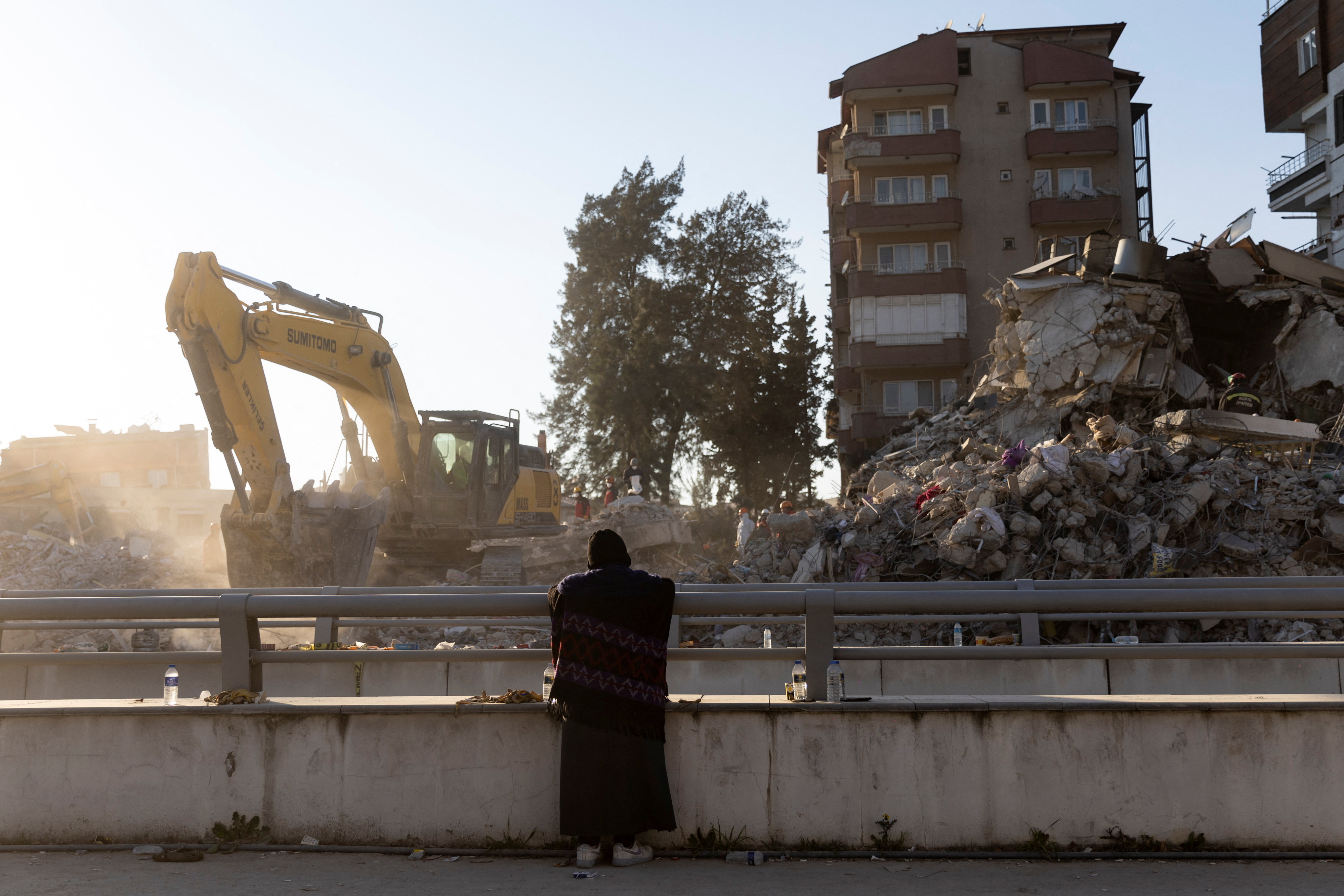 A woman waits while search teams dig through the rubble of a collapsed building in the aftermath of the deadly earthquake in Hatay, Turkey