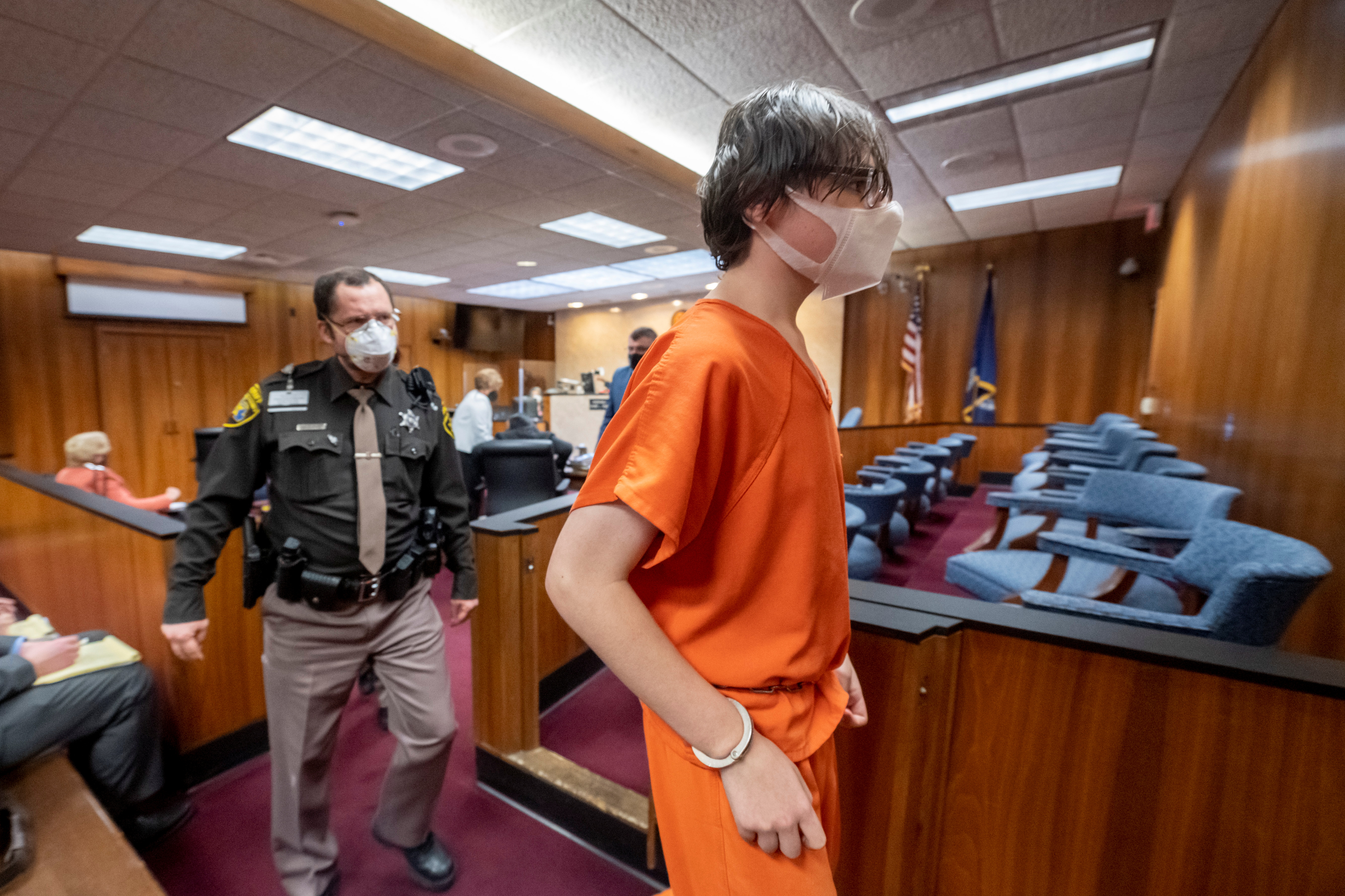 A teenager in an orange jump suit is escorted through court by law enforcement