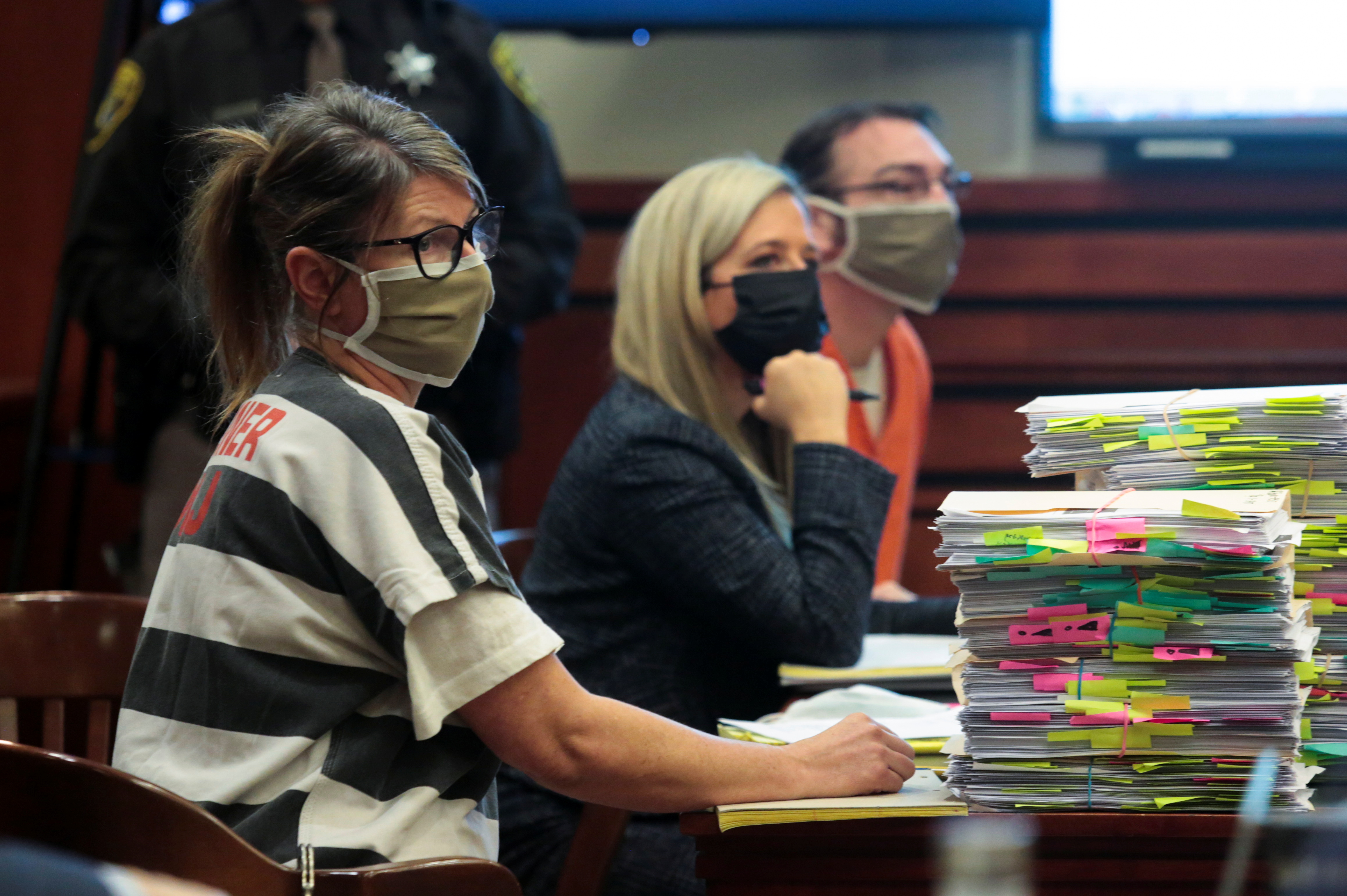 A woman in a striped jump suit and a man in an orange jump suit sit on either side of a lawyer