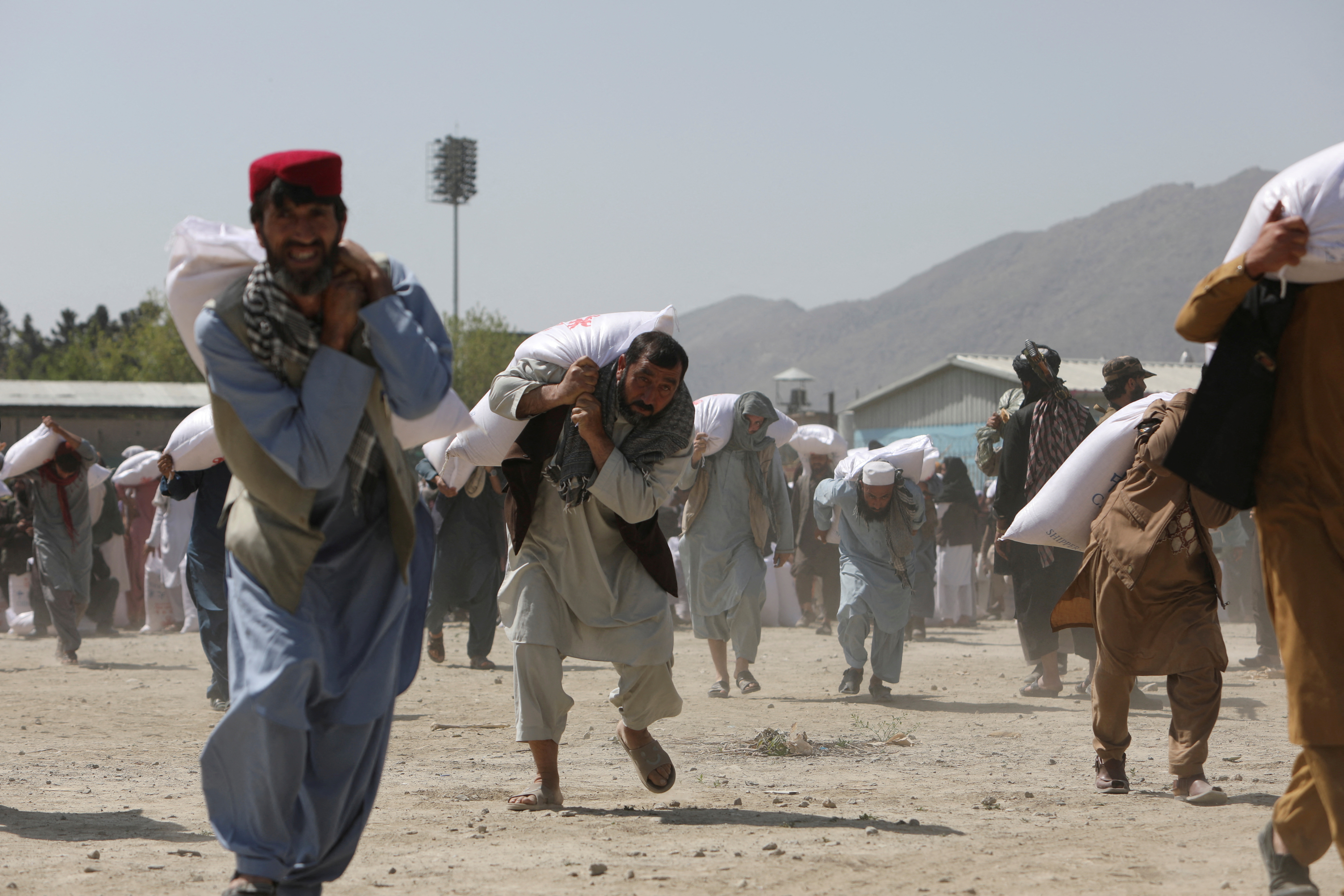 Afghan people carry sacks of rice, given out as part of humanitarian aid sent by China to Afghanistan, at a distribution centre in Kabul, Afghanistan, April 7, 2022. REUTERS/Ali Khara TPX IMAGES OF THE DAY