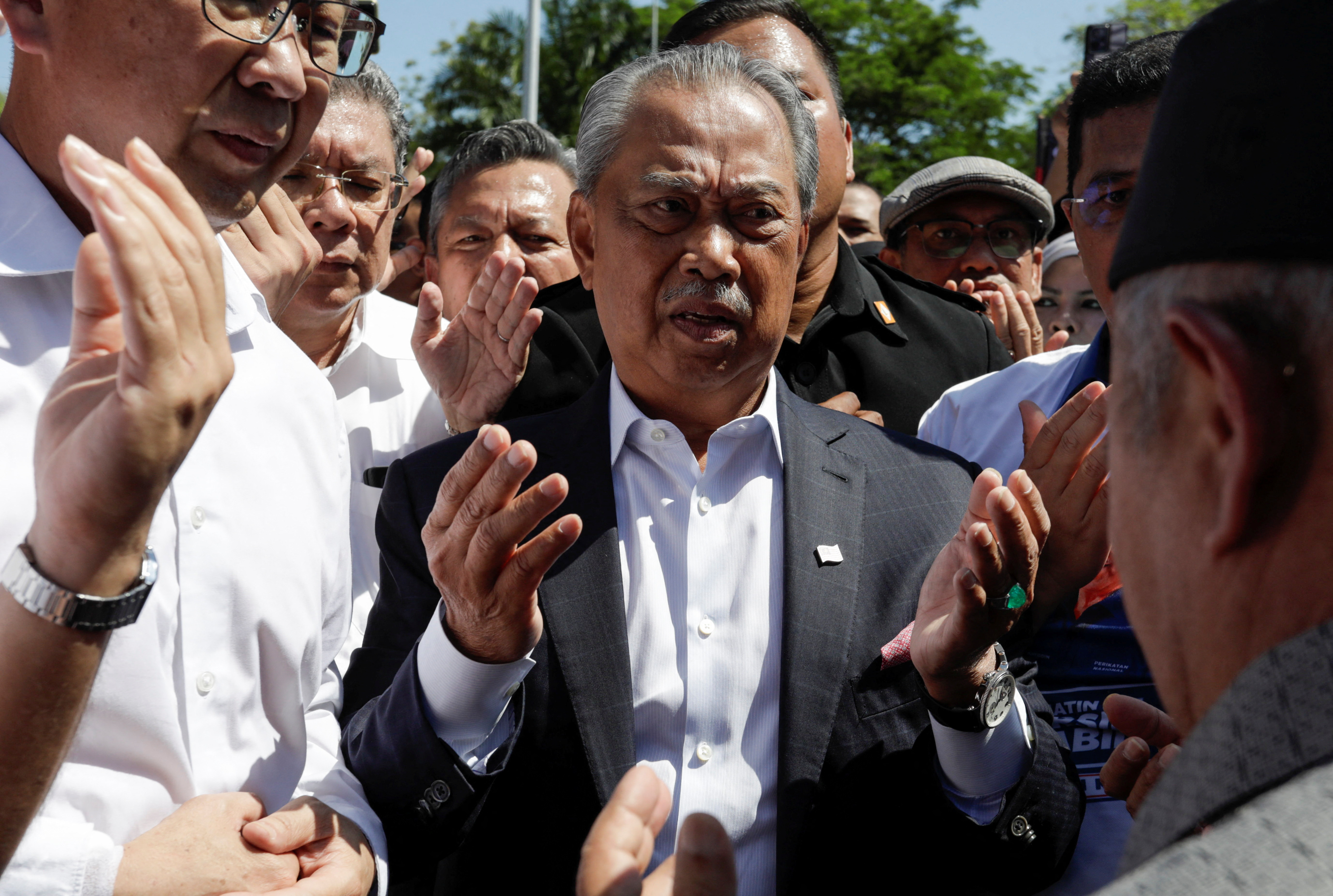 Muhyiddin Yassin praying before he heads into the MACC for questioning. He is surrounded by supporters.
