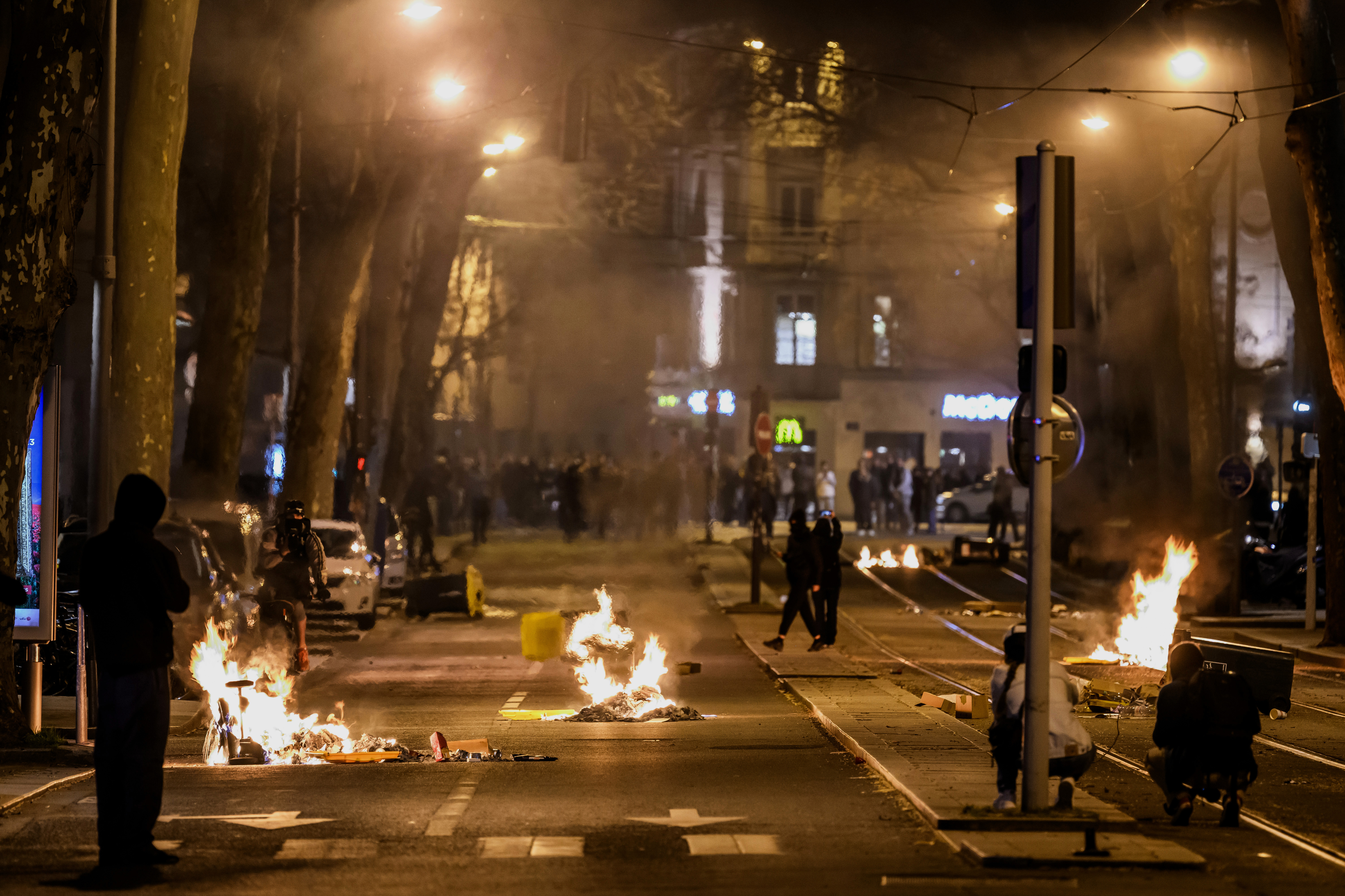 People walk past burning rubbish during a demonstration in Lyon, eastern France, on March 20, 2023