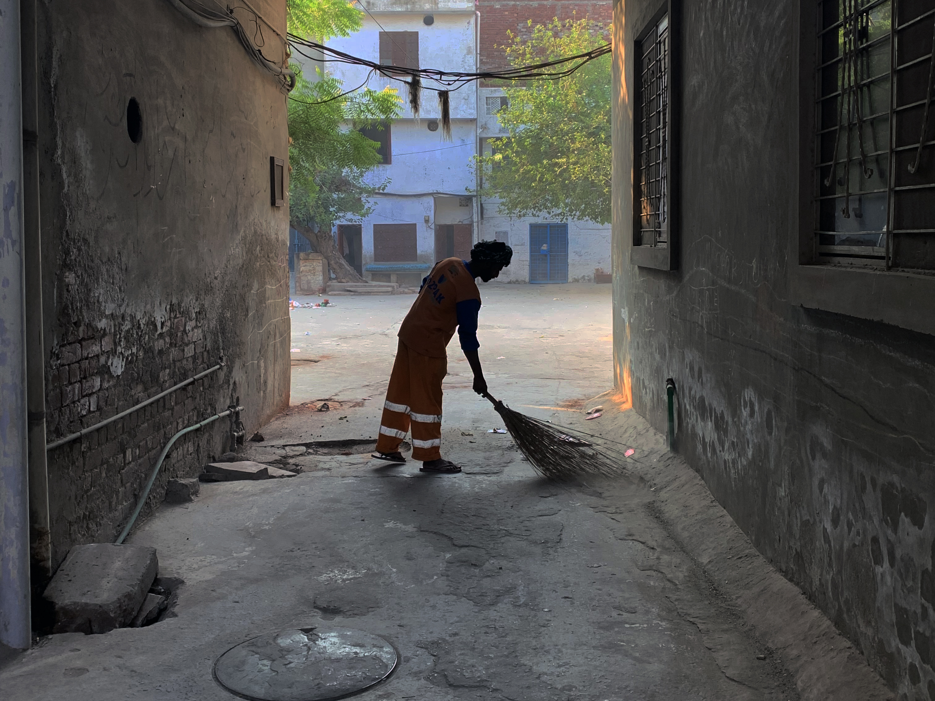 A photo of a person sweeping in an alleyway between two houses.