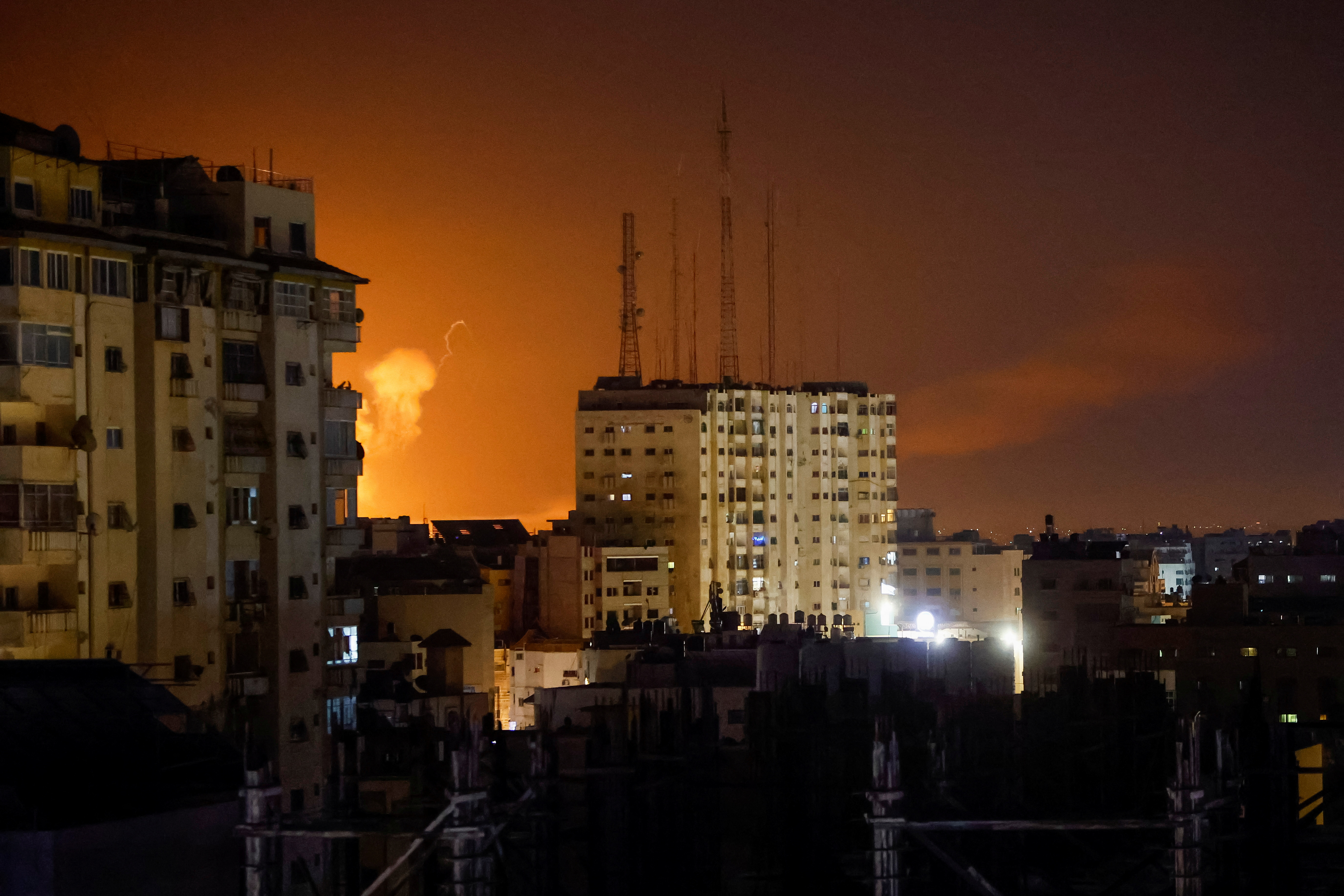 A city skyline with explosions seen lighting up the night sky.