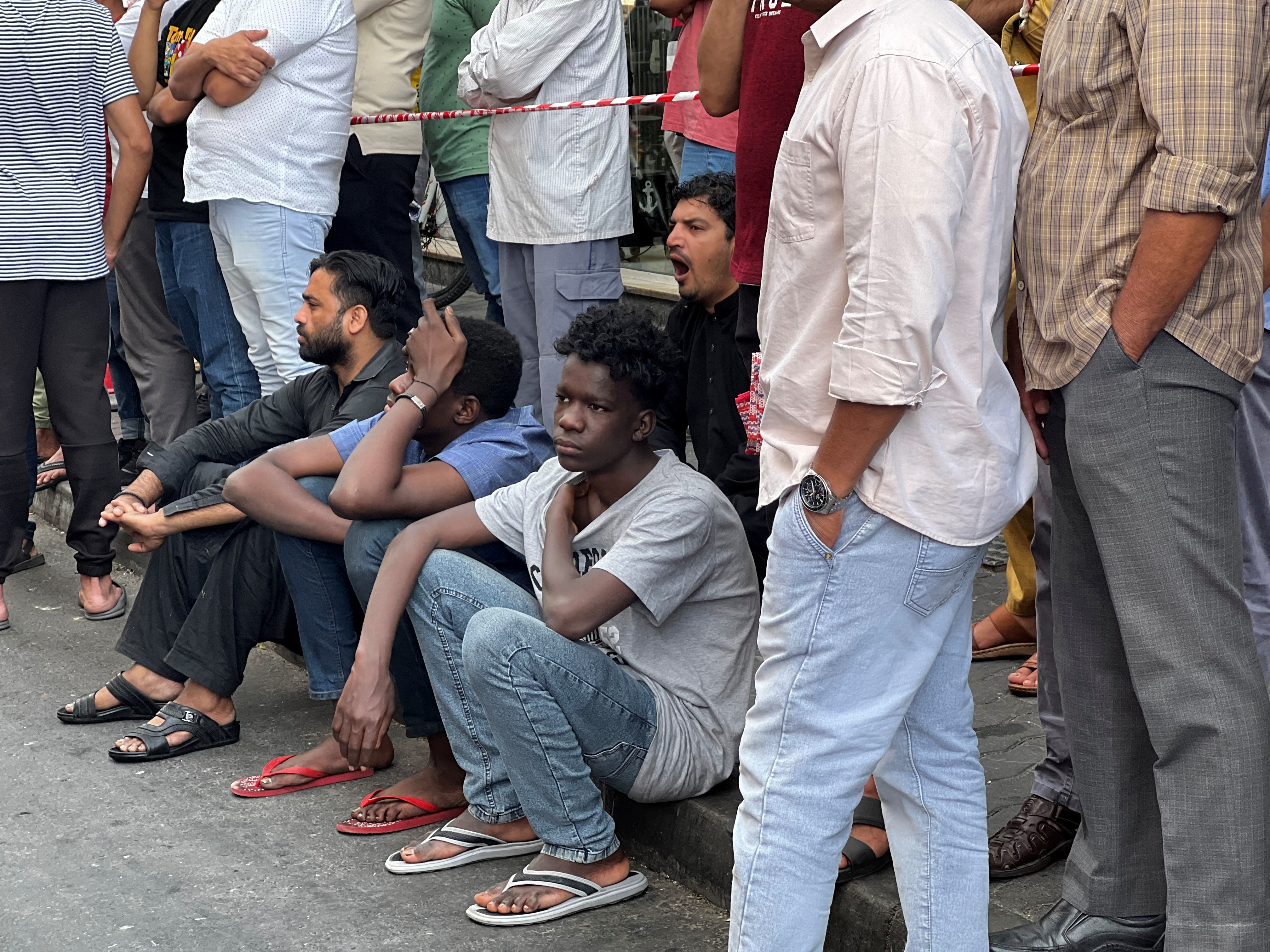 People, including residents, stand outside a residential building that was devastated by a fire