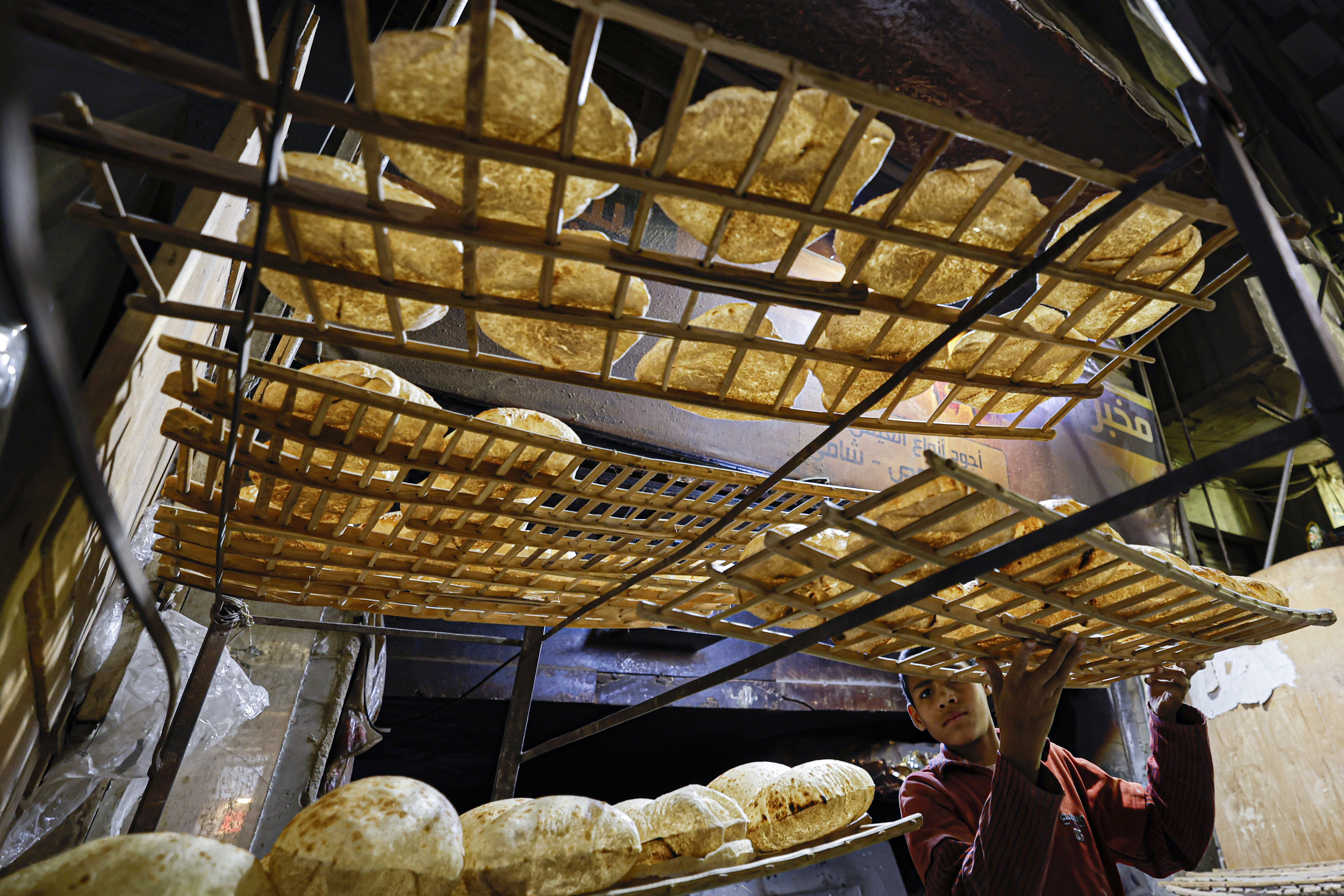 A young worker stacks trays of freshly-baked bread at a bakery in Cairo