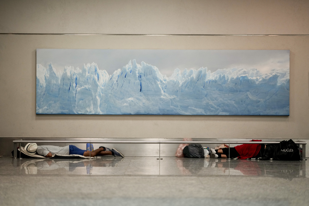 Homeless men sleep below a photo of the Perito Moreno Glacier at the Jorge Newbery international airport in Buenos Aires, April 6