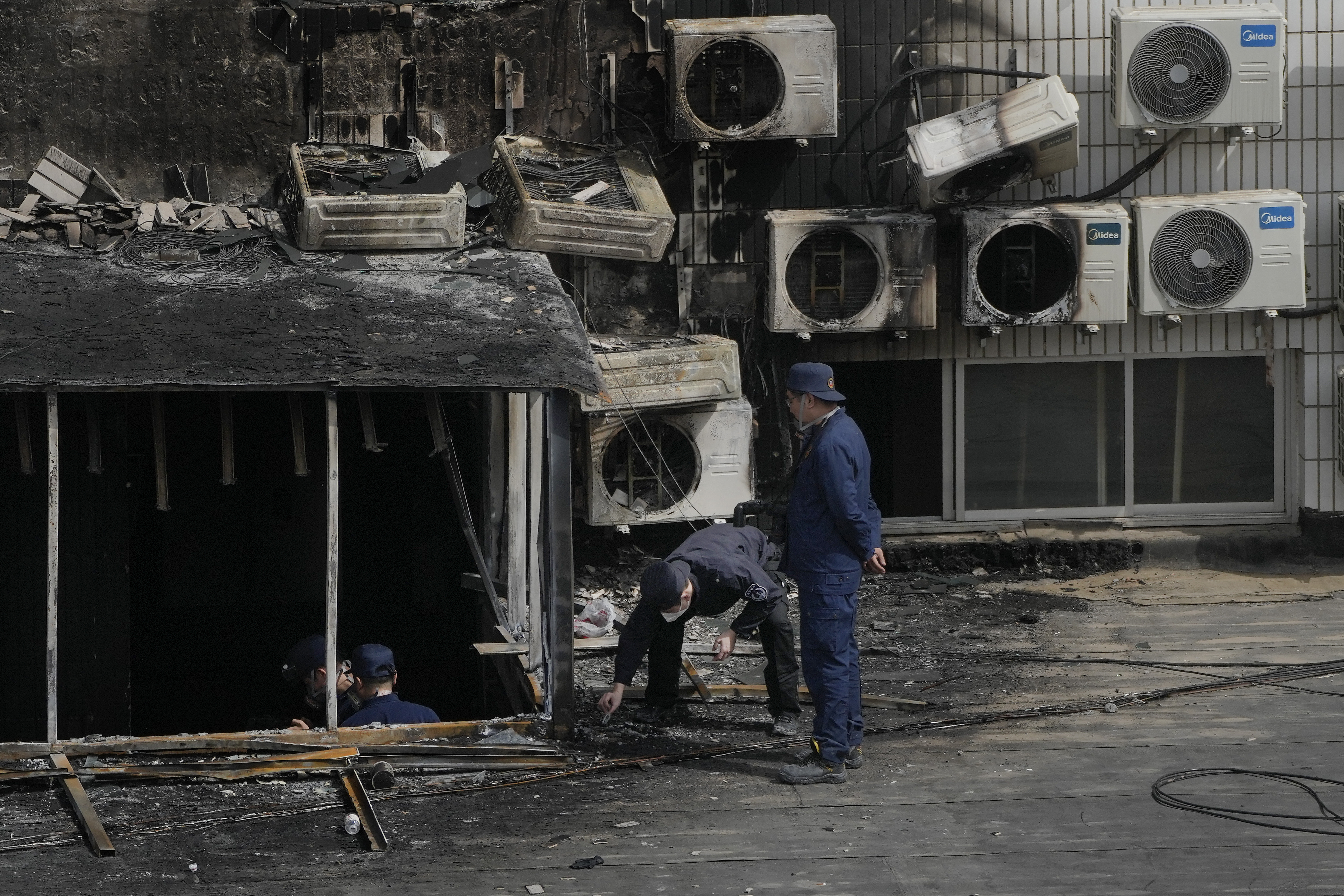 An investigator bends down to look at something on the ground at the scene of the Beijing hospital fire. There are numerous airconditioners on the wall of the building and some have been destroyed by the fire. There is soot on the walls.
