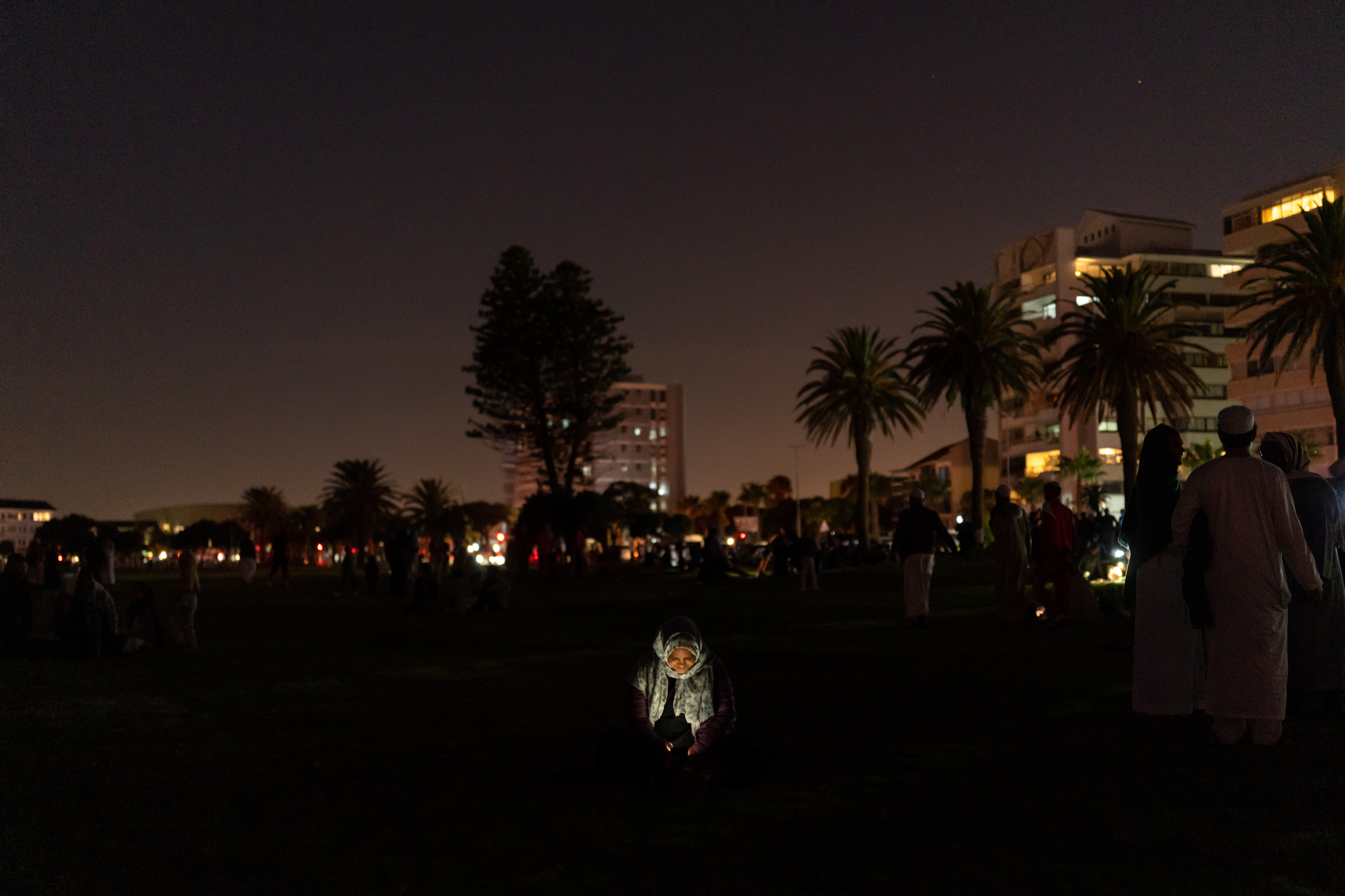 A woman's face is lit by the light of her mobile phone, as people leave the moon sighting