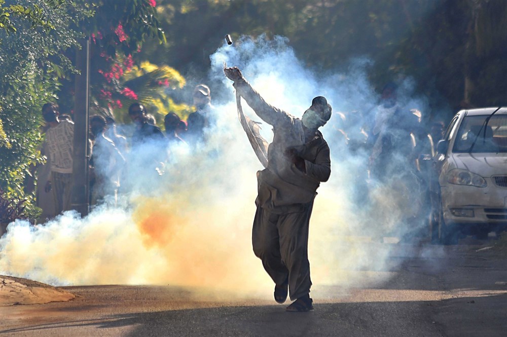 A man throws a tear gas canister back towards security personnel during clashes in Karachi, May 10, 2023