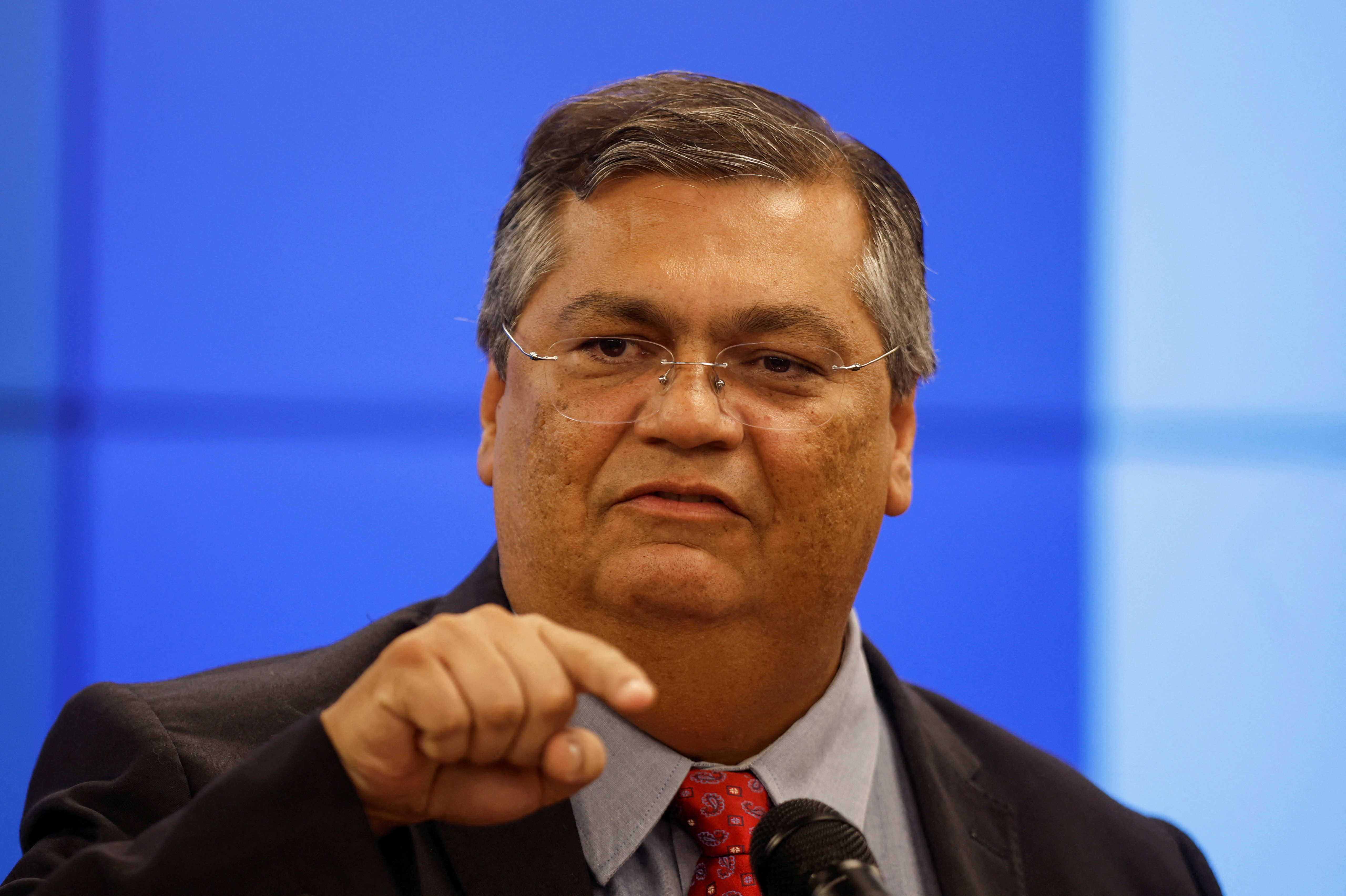 Flávio Dino points against a blue backdrop