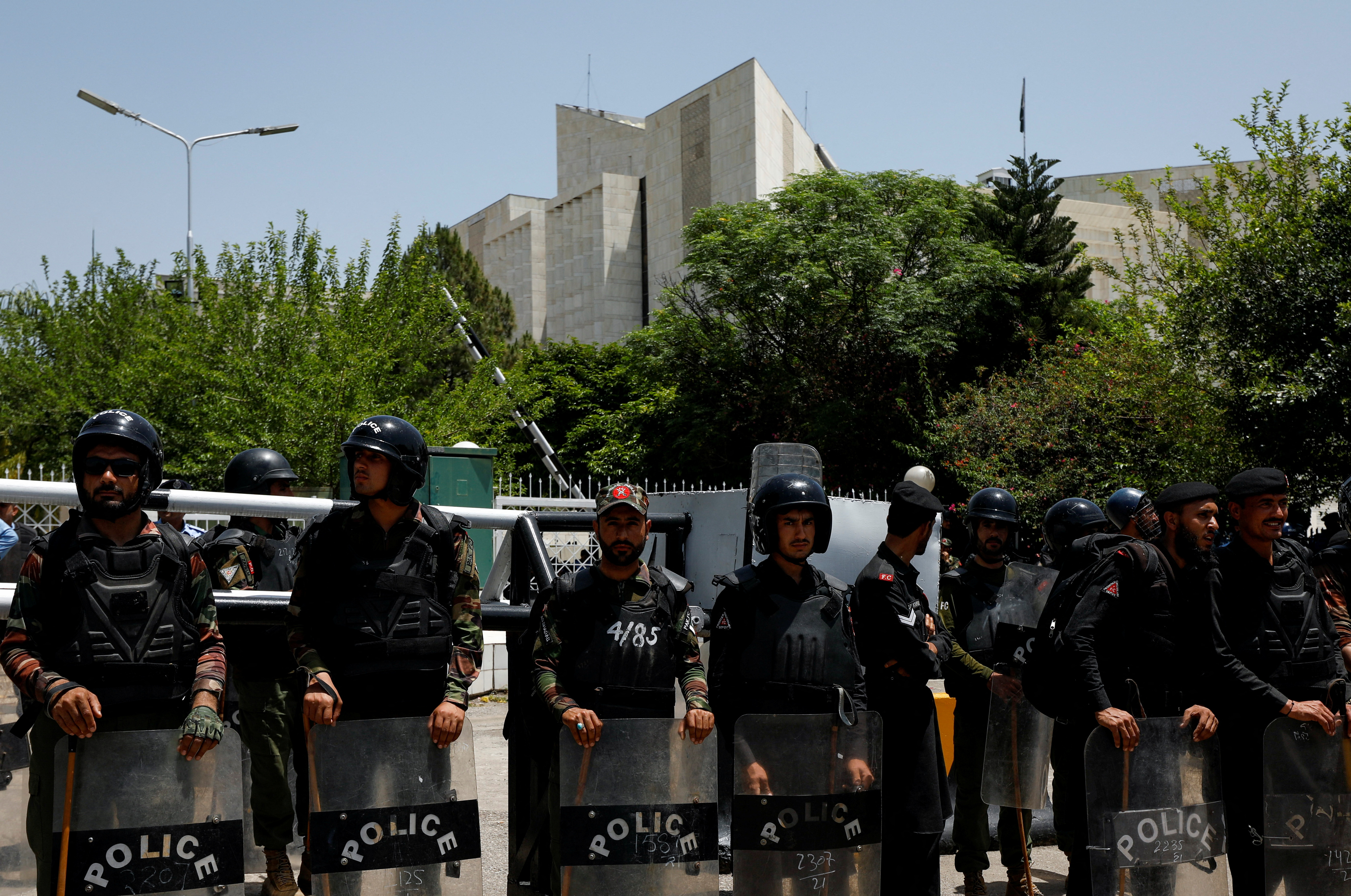 Police officers stand guard as supporters of Pakistan Democratic Movement (PDM), a coalition of political parties, gather in front of the Supreme Court of Pakistan to protest against the granting of bail in several cases to Pakistan's former Prime Minister Imran Khan, in Islamabad