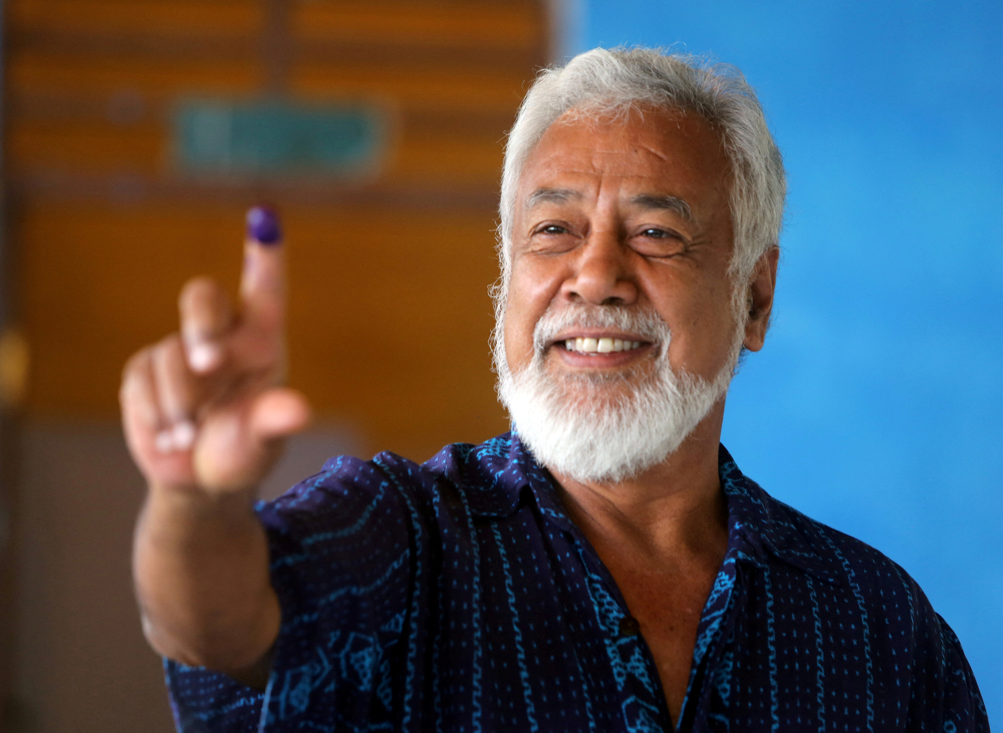 Xanana Gusmao holding up his ink-stained finger after voting. He is smiling.