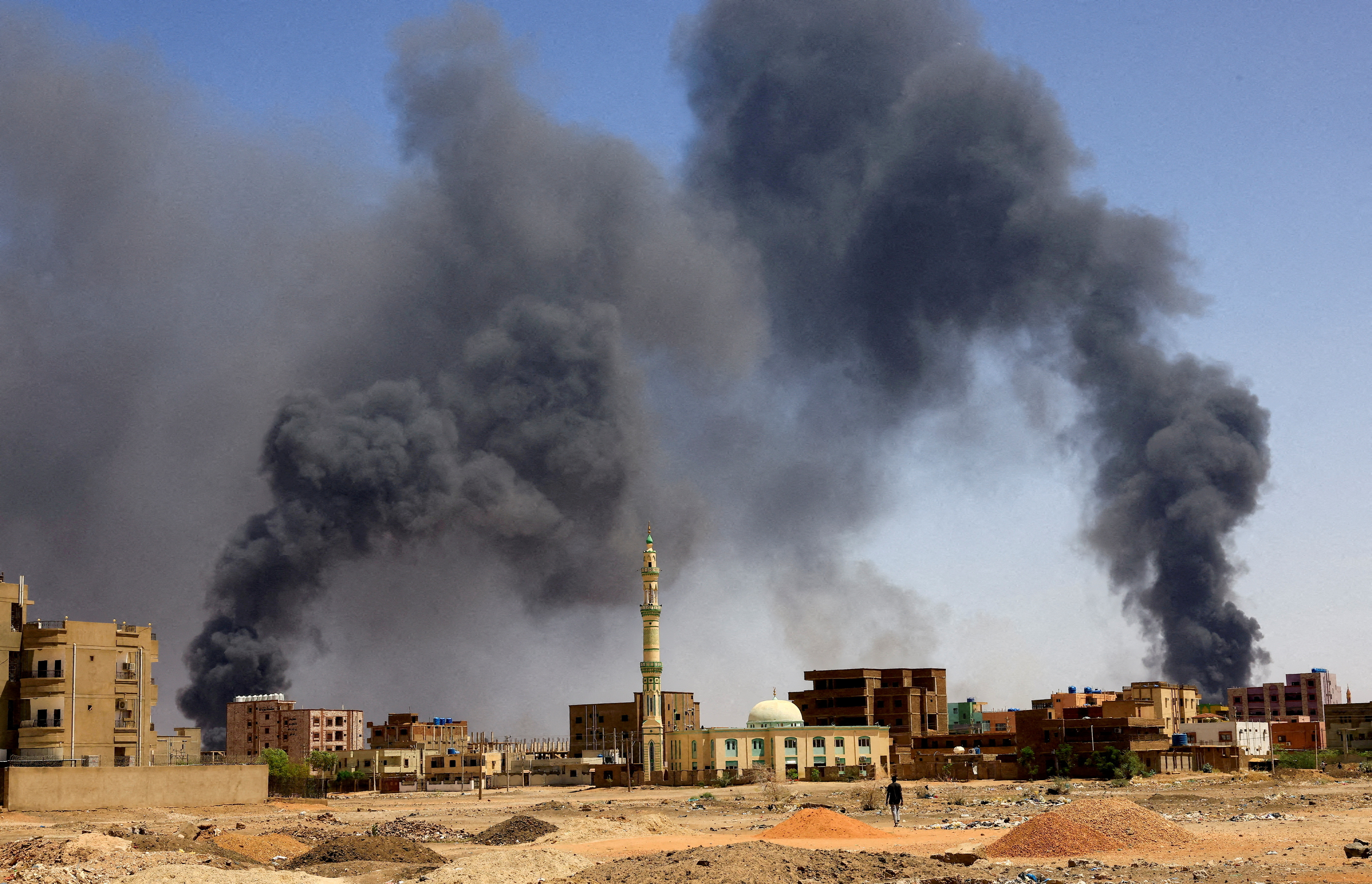FILE PHOTO: A man walks while smoke rises above buildings after aerial bombardment, during clashes between the paramilitary Rapid Support Forces and the army in Khartoum North, Sudan, May 1, 2023. REUTERS/Mohamed Nureldin Abdallah/File Photo