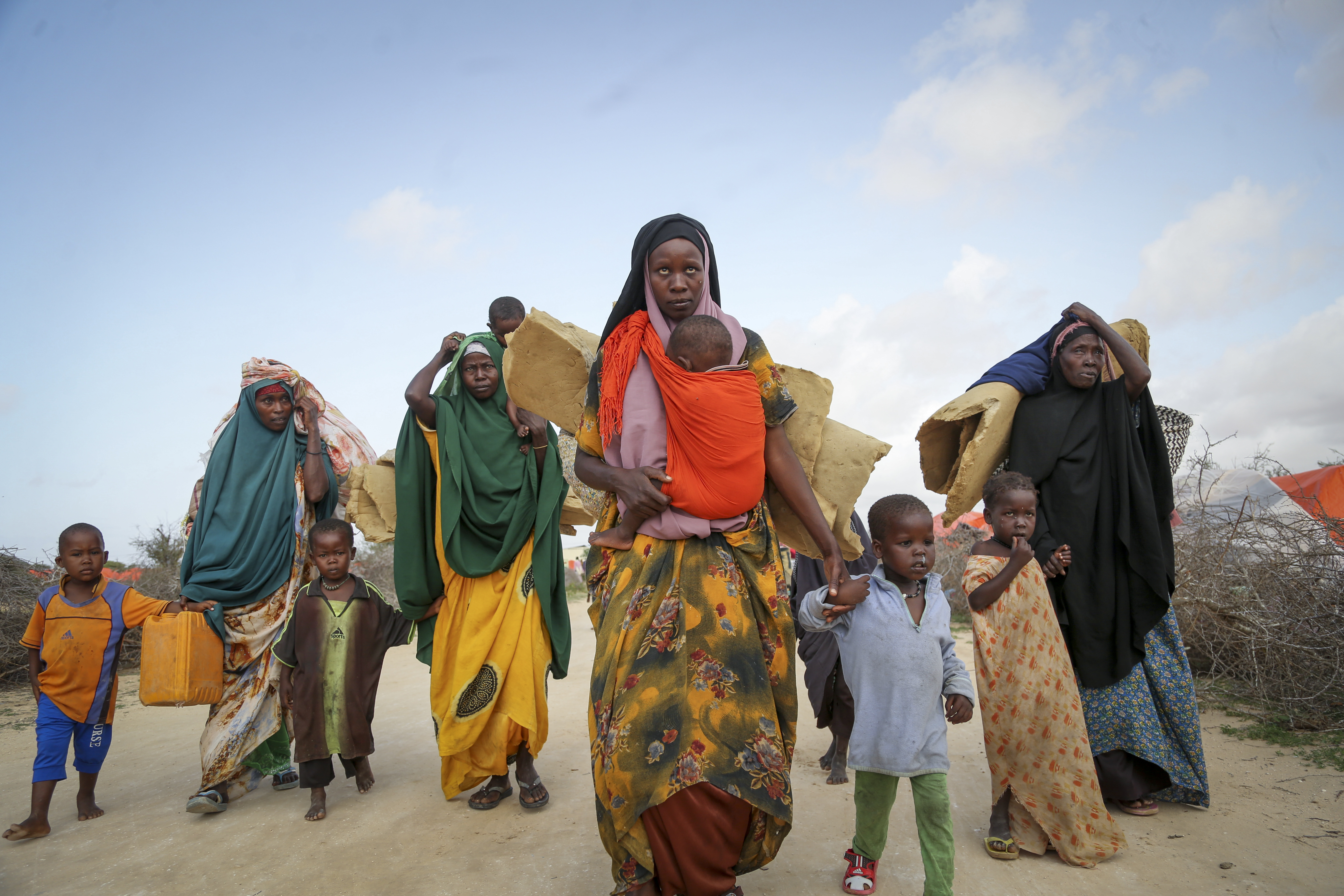 FILE - Somalis who fled drought-stricken areas carry their belongings as they arrive at a makeshift camp for the displaced on the outskirts of Mogadishu, Somalia, June 30, 2022. Tens of millions of people are being uprooted by natural disasters due to the impact of climate change, though the world has yet to fully recognize climate migrants or come up with a formalized mechanism to assess their needs and help them. (AP Photo/Farah Abdi Warsameh, File)