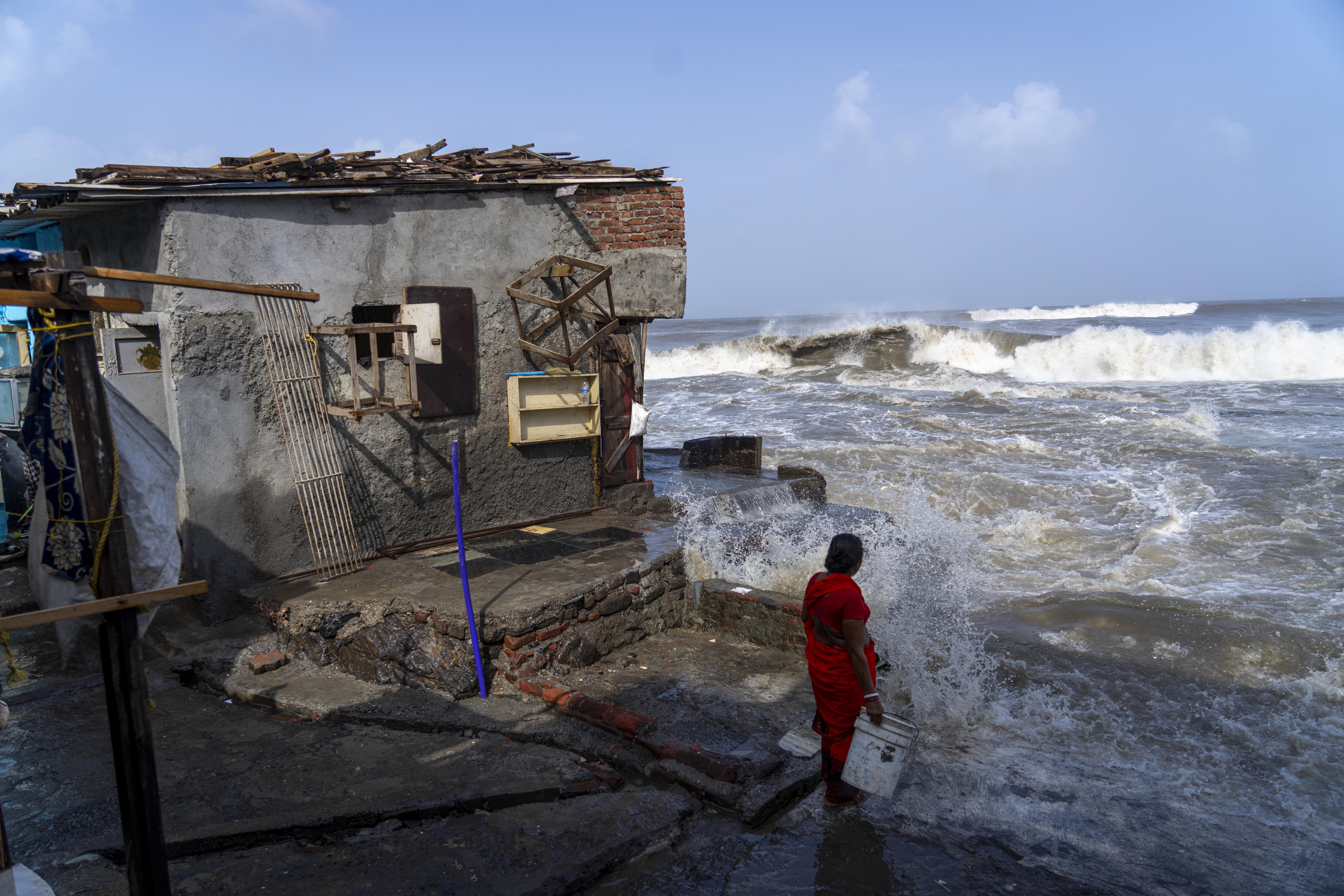 A woman stands next to her house as large waves hit Mumbai