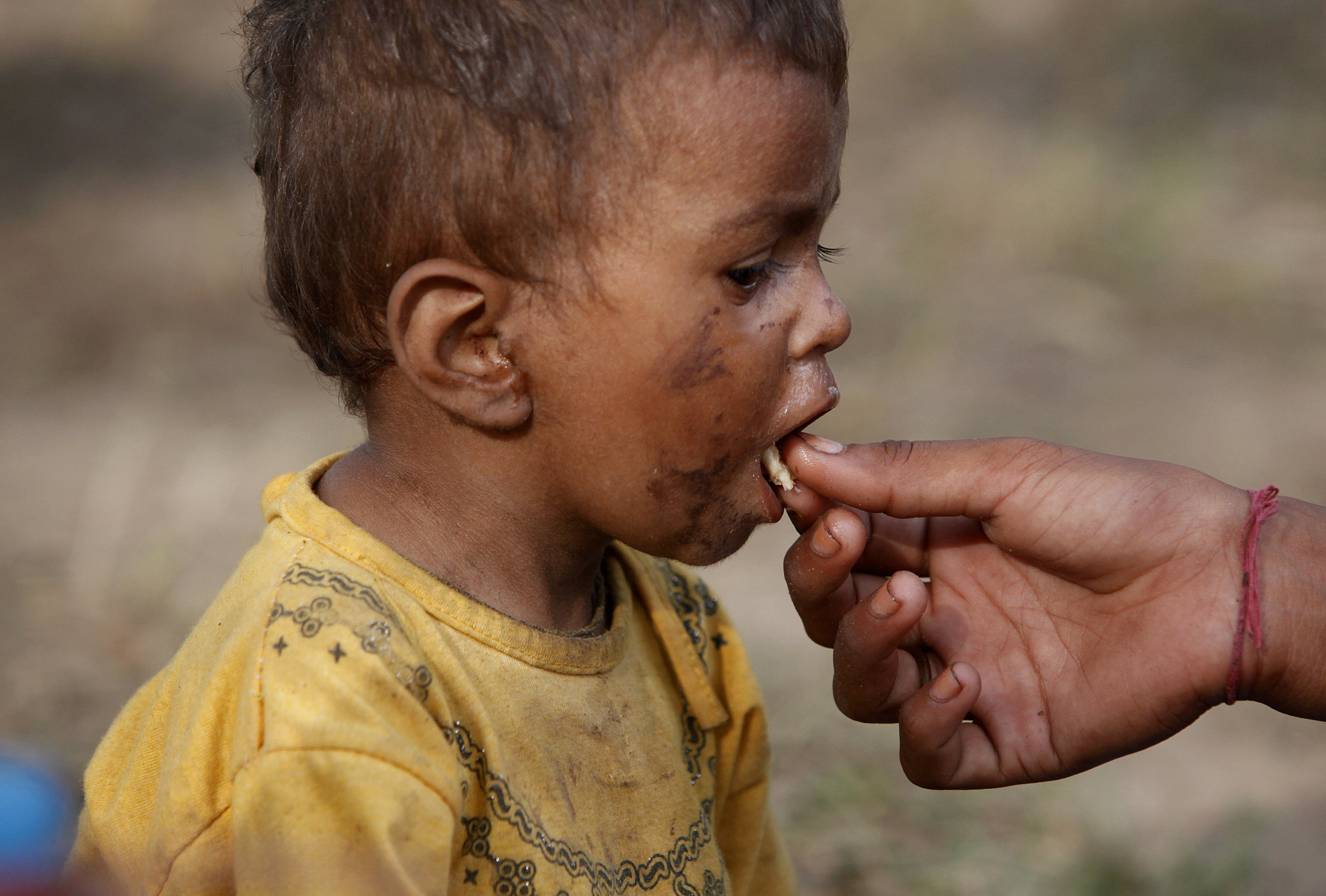 A two-year-old flood victim is fed by his sister as they take refuge with his family in a public park in Thatta, in Pakistan's Sindh province