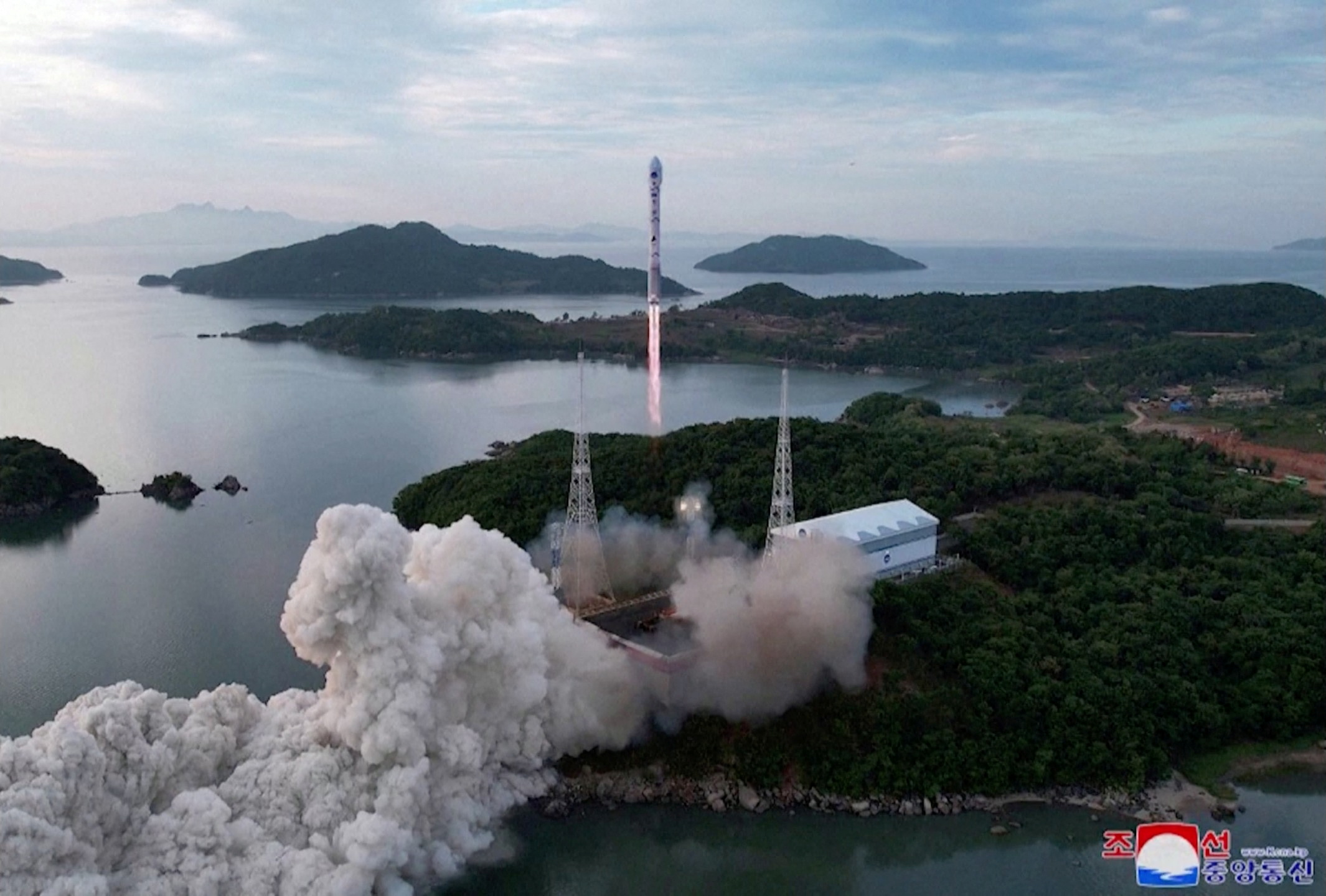 A photo showing the launch of North Korea's Chollima rocket. There are clouds of white smoke, and hilly islands around the launch site.