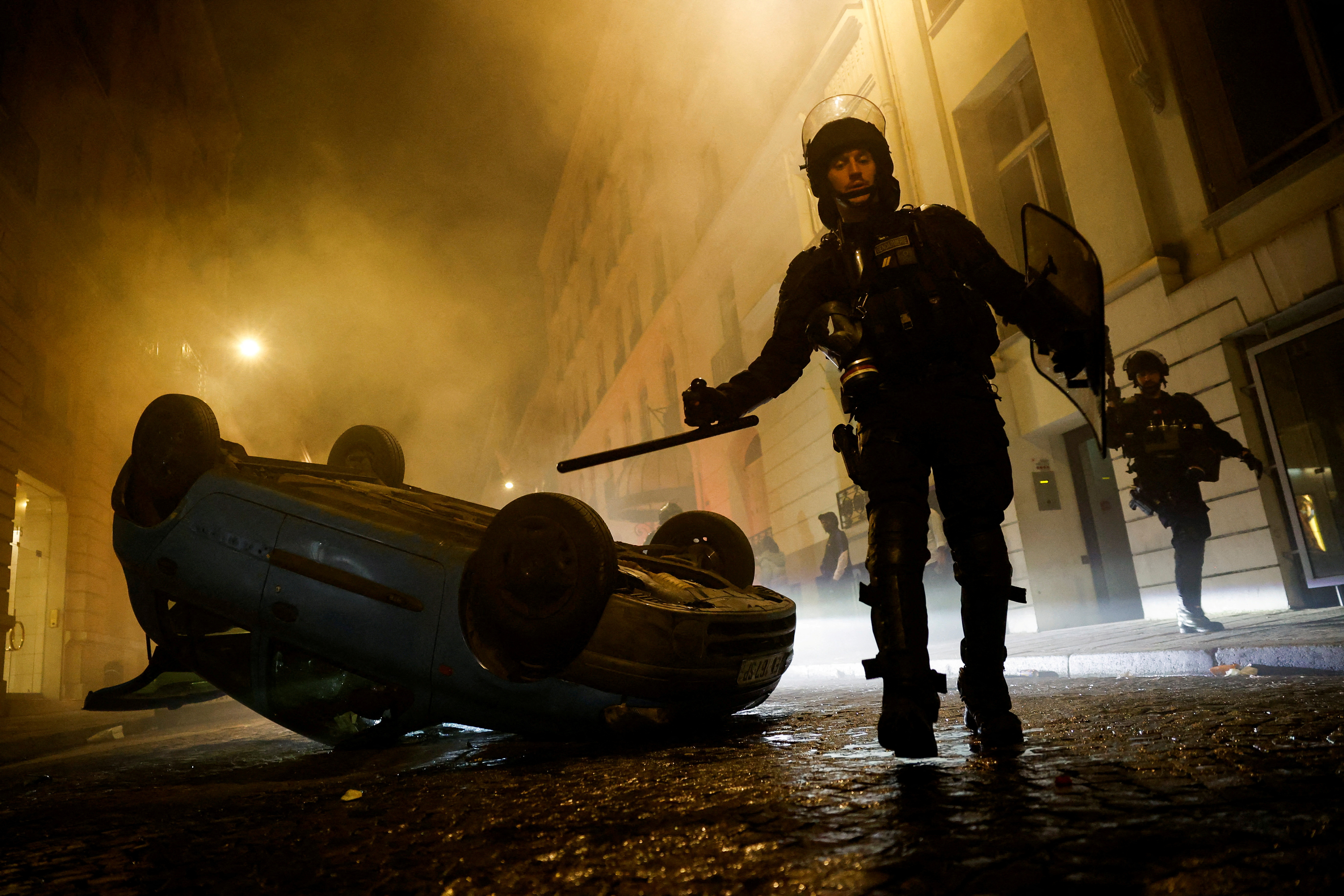 French riot police officers walk next to a vehicle upside down during the fifth day of protests following the death of Nahel, a 17-year-old teenager killed by a French police officer in Nanterre during a traffic stop, in Paris, France, July 2, 2023. REUTERS/Juan Medina TPX IMAGES OF THE DAY