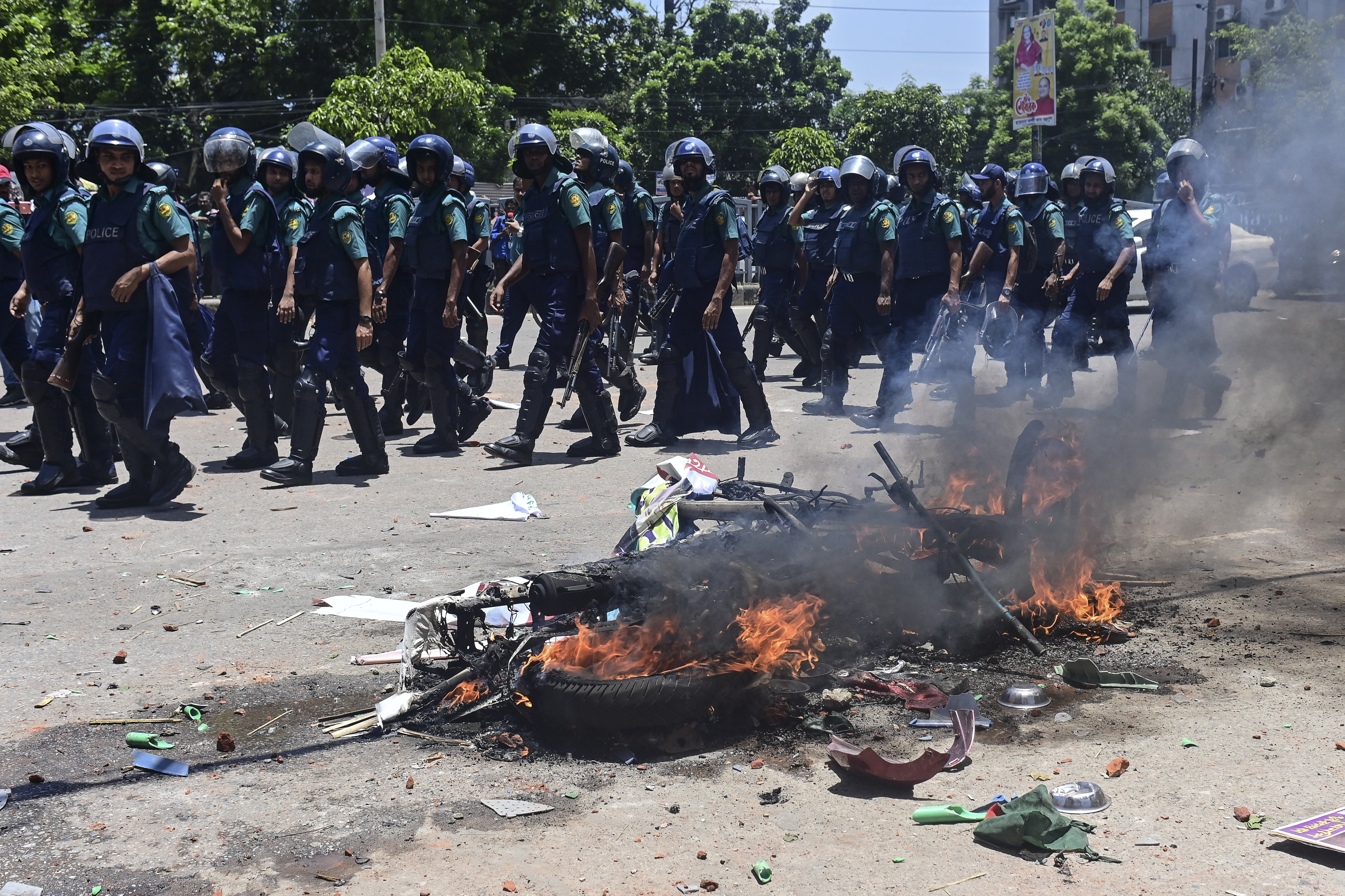 Bangladesh police walk past a motorbike set on fire during the march in Dhaka
