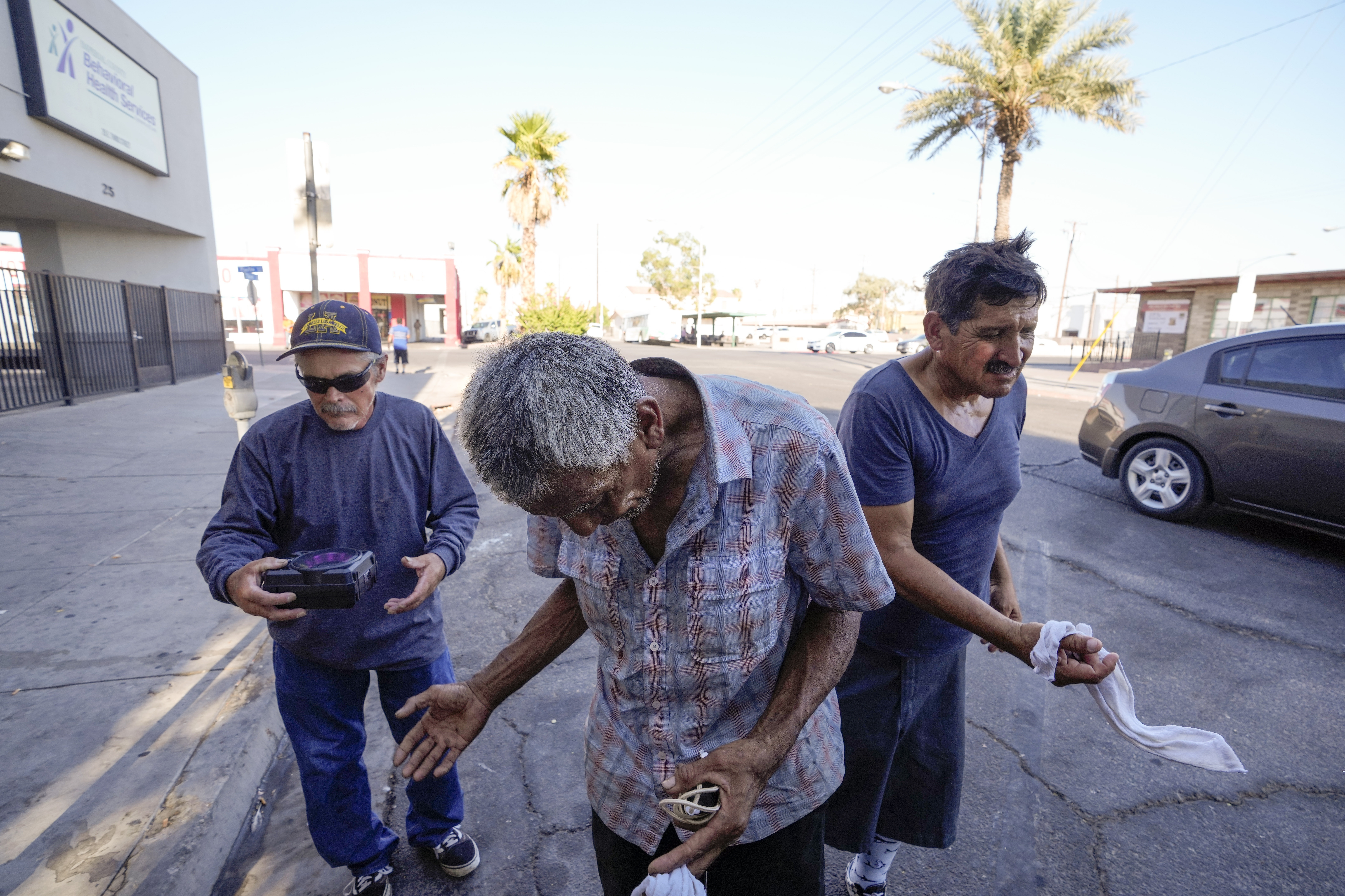 Three men, who are homeless, react as they are given cold, wet towels