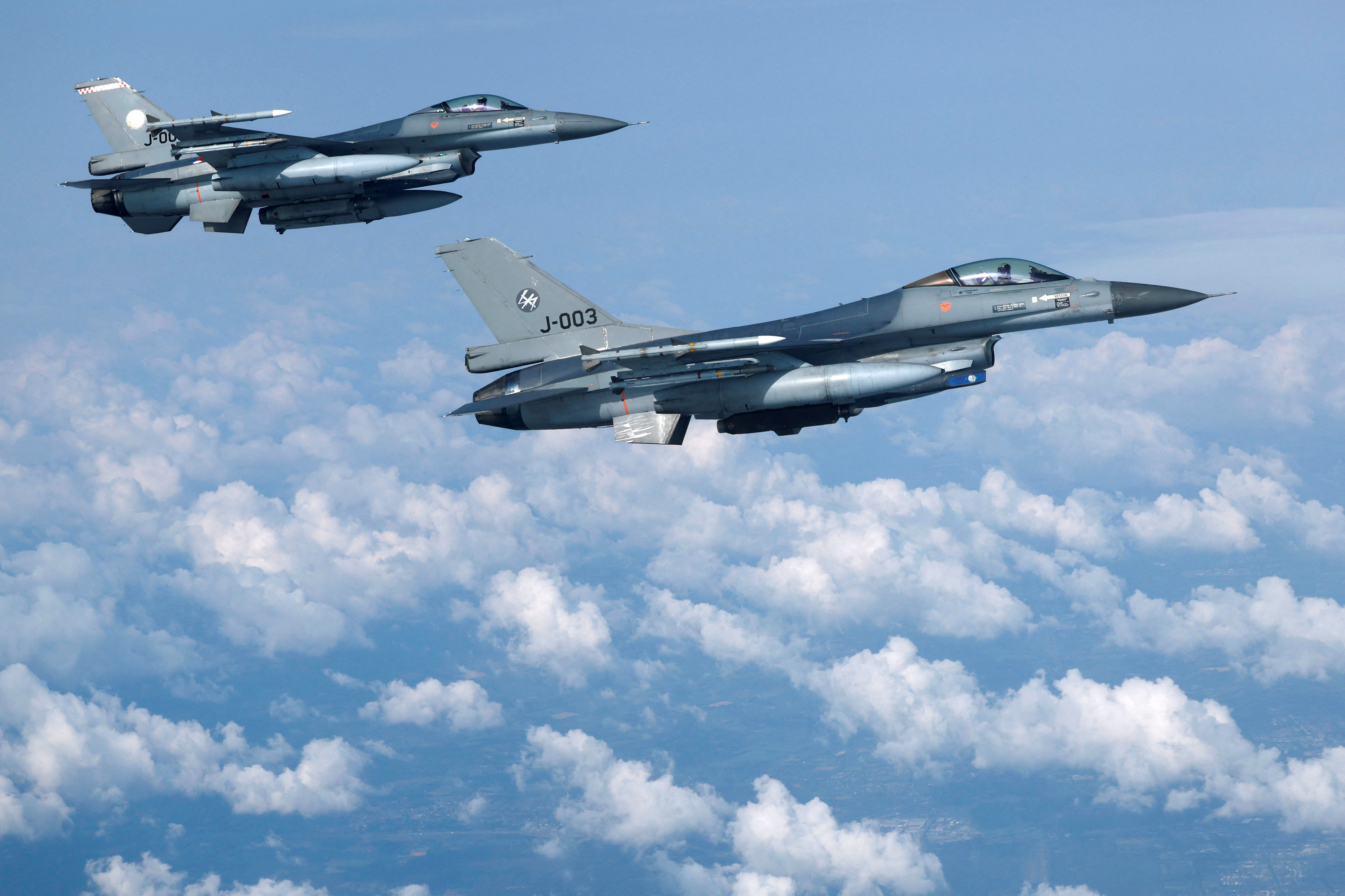 Two F-16 fighter jets from the Netherlands in the air. There are clouds beneath them.