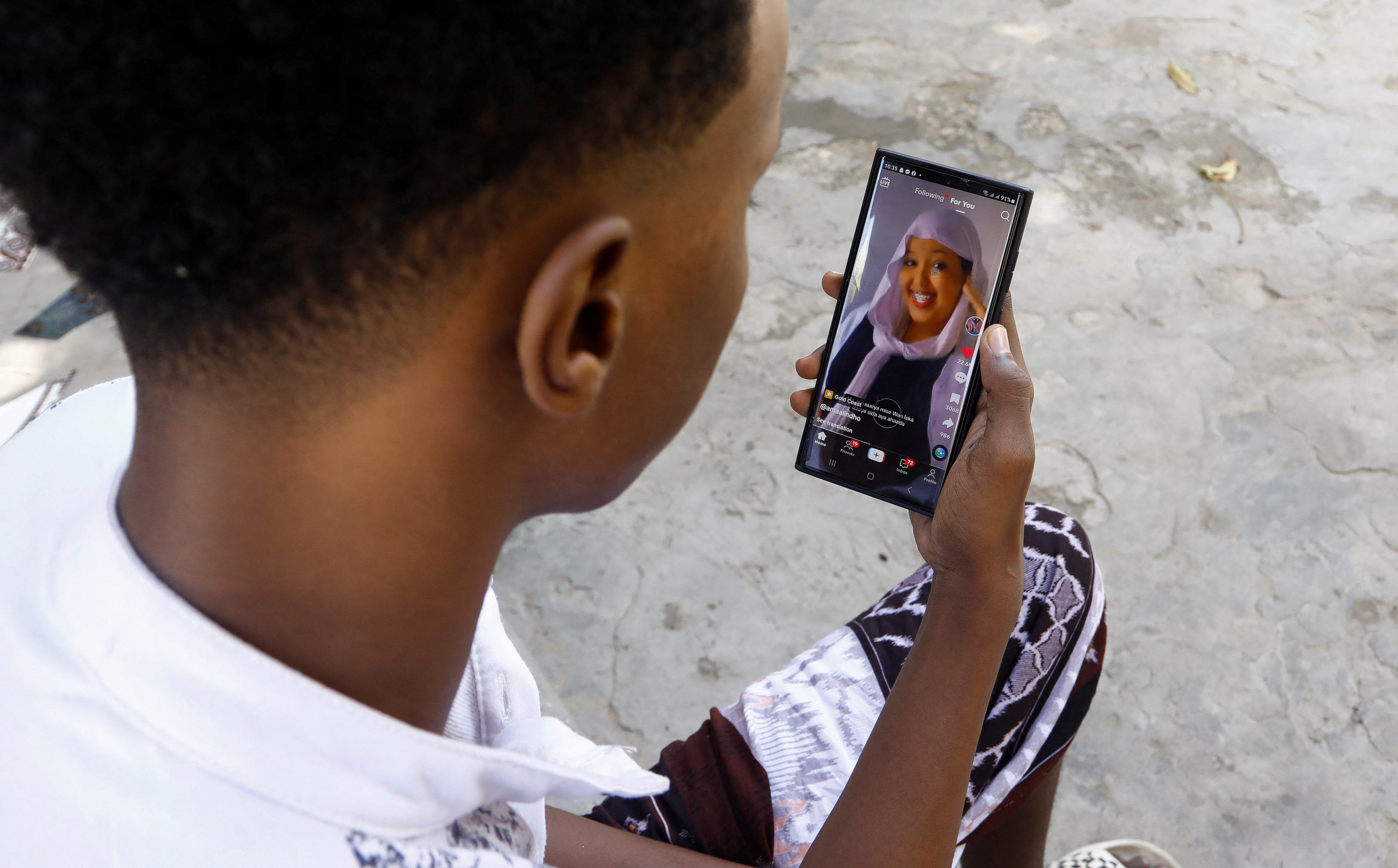 Abdulahi Ahmed uses his mobile phone to watch a video on social media app TikTok, outside his home in Waberi district of Mogadishu, Somalia