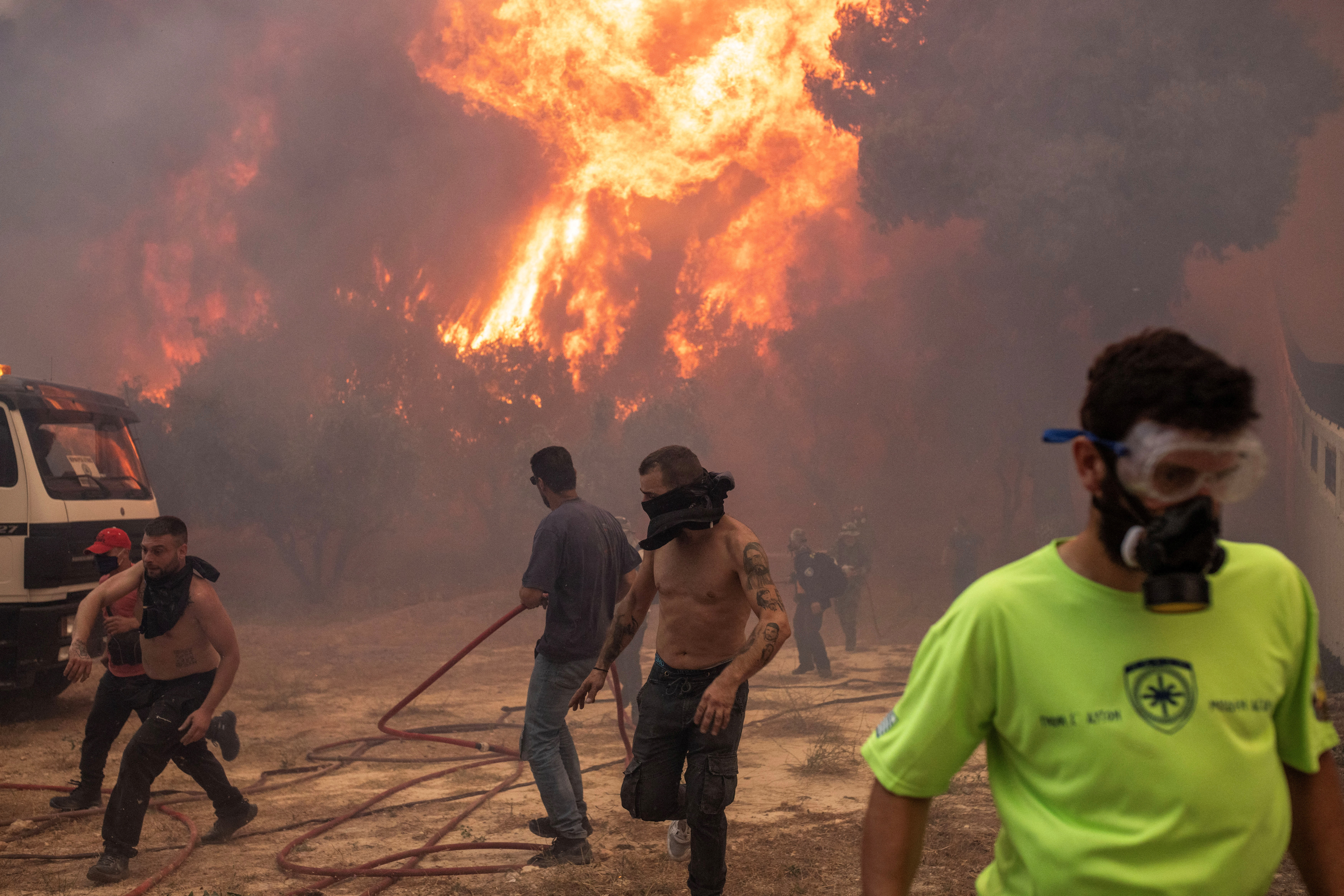 Firefighters and volunteers flee as a wildfire burns in the village of Hasia, near Athens