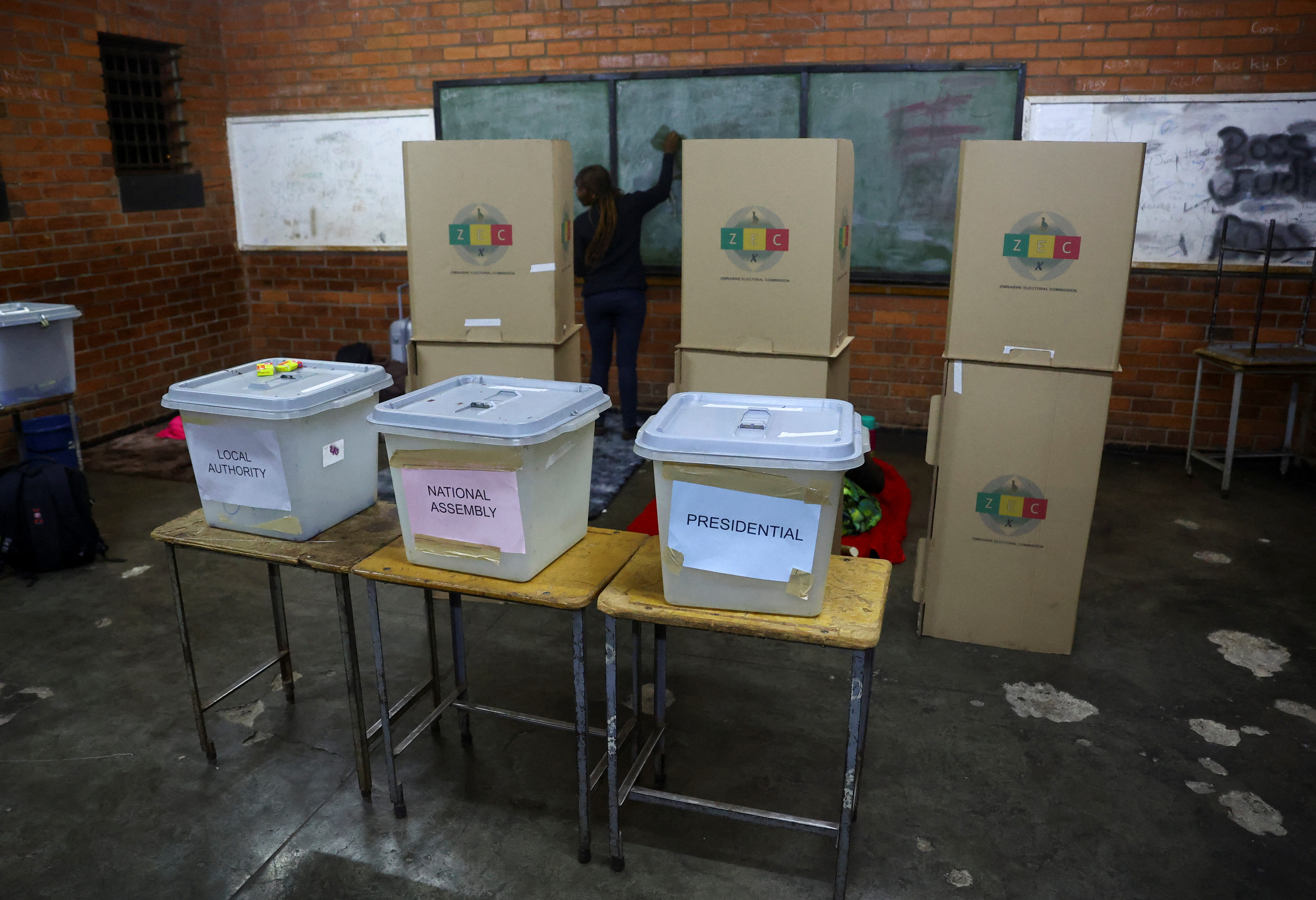 A worker cleans a chalk board behind ballot boxes, ahead of the presidential elections in Warren Park, Harare
