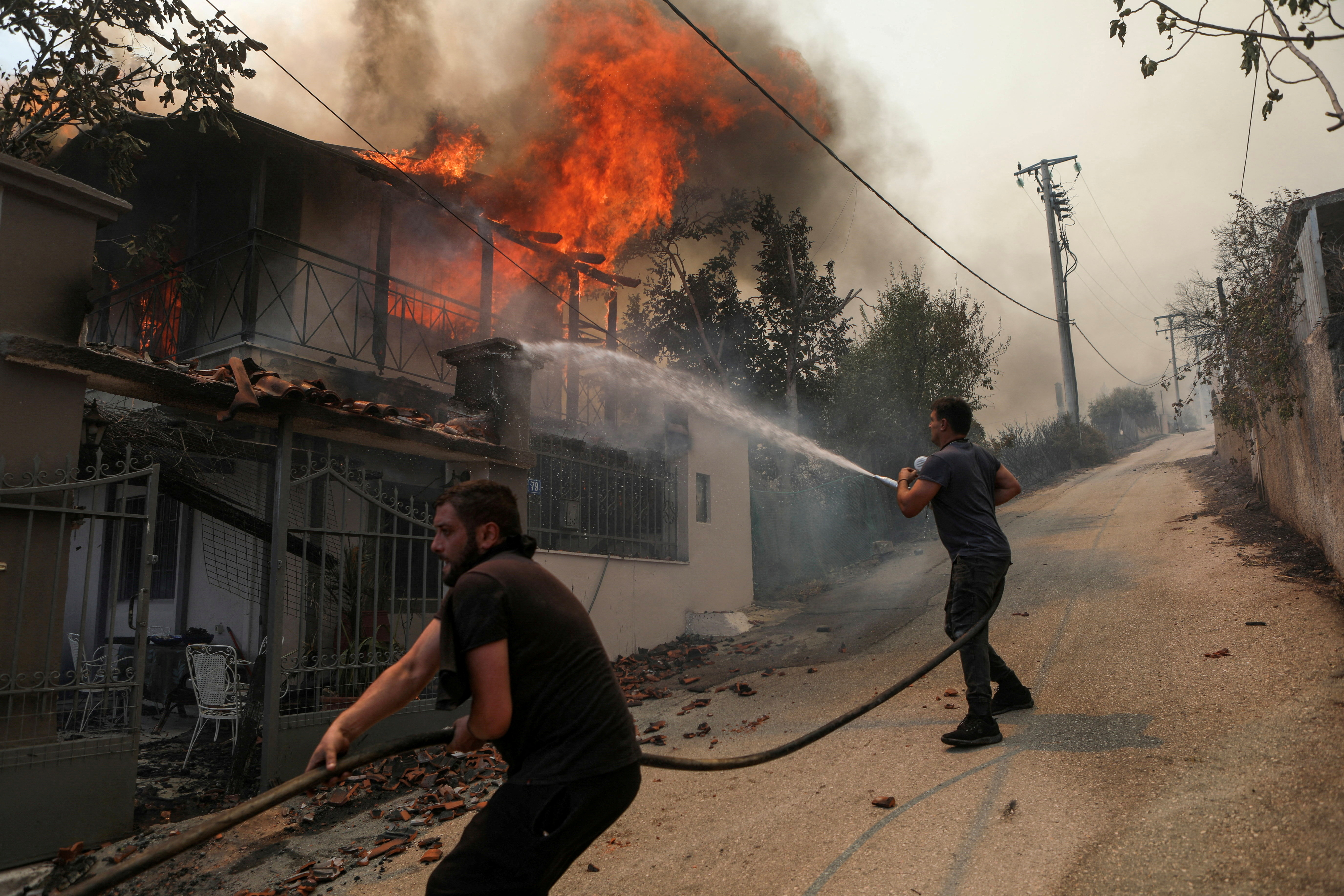 Volunteers try to extinguish a fire burning a house, as a wildfire burns in Menidi, near Athens