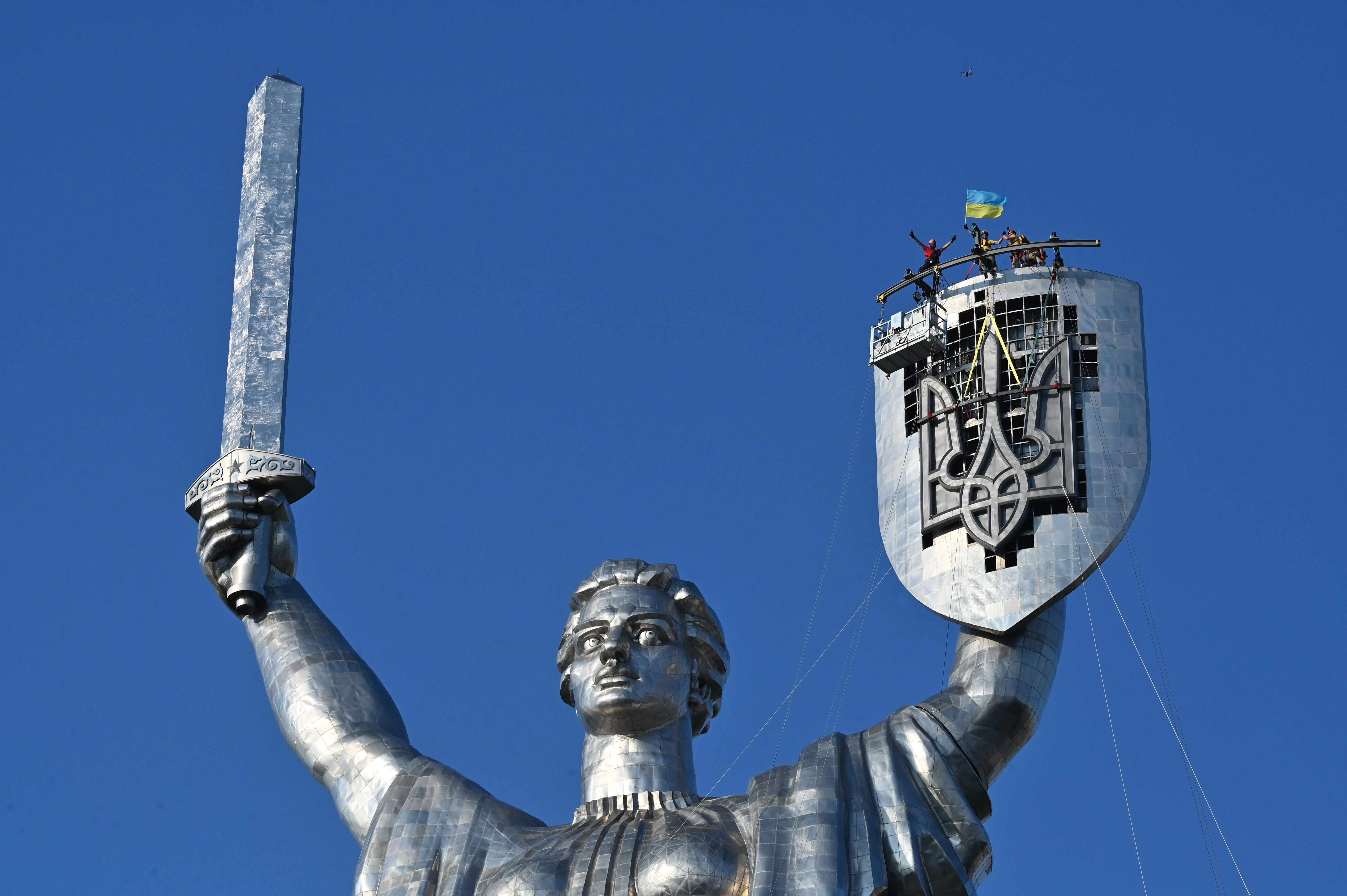 Steeplejacks wave a flag after they installed the Ukrainian official coat of arms on the shield of the 62-meter Motherland Monument in Kyiv, on August 6, 2023.