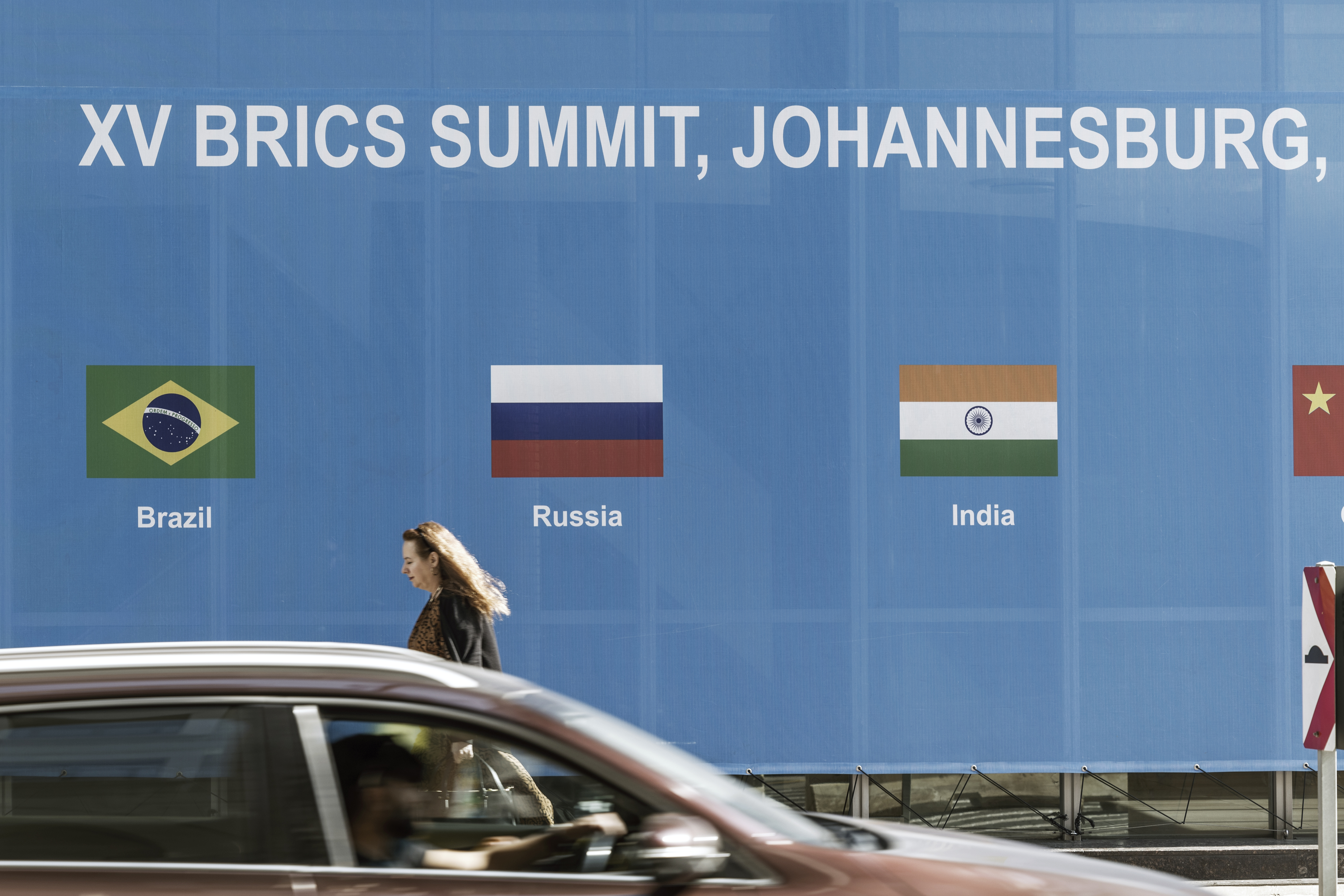 A woman walks past a poster for the 2023 BRICS Summit at the Sandton Convention Centre in Sandton, Johannesburg, on August 20, 2023. - The BRICS countries, an acronym of the five members Brazil, Russia, India, China and South Africa, meet for three days for a summit in Johannesburg starting August 22, 2023. (Photo by MARCO LONGARI / AFP)