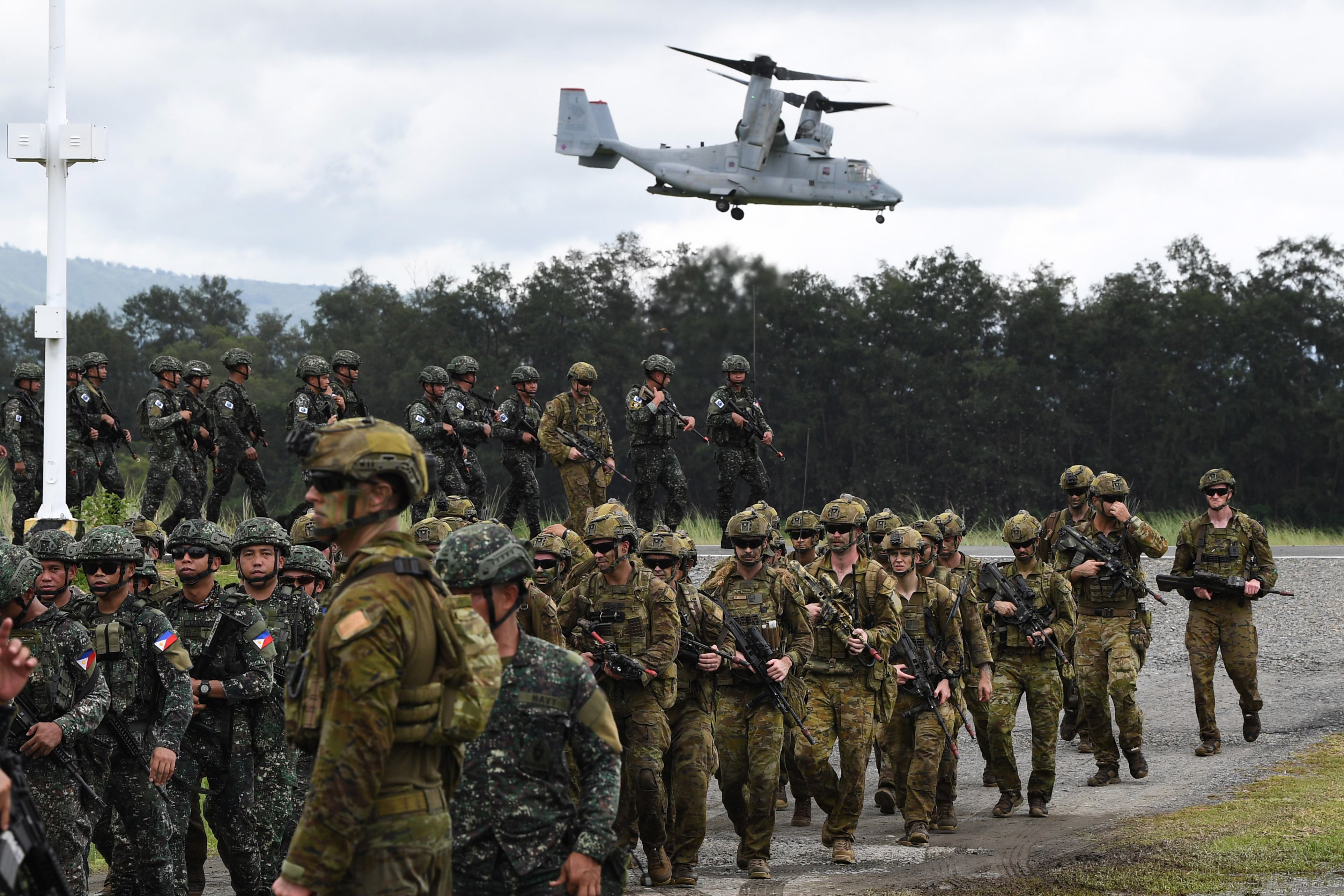 Philippine and Australian soldiers march in formation while a US Marines V-22 Osprey hovers above during military exercise in San Antonio in Zambales province, north of Manila on August 25, 2023 [Ted Aljibe/AFP]
